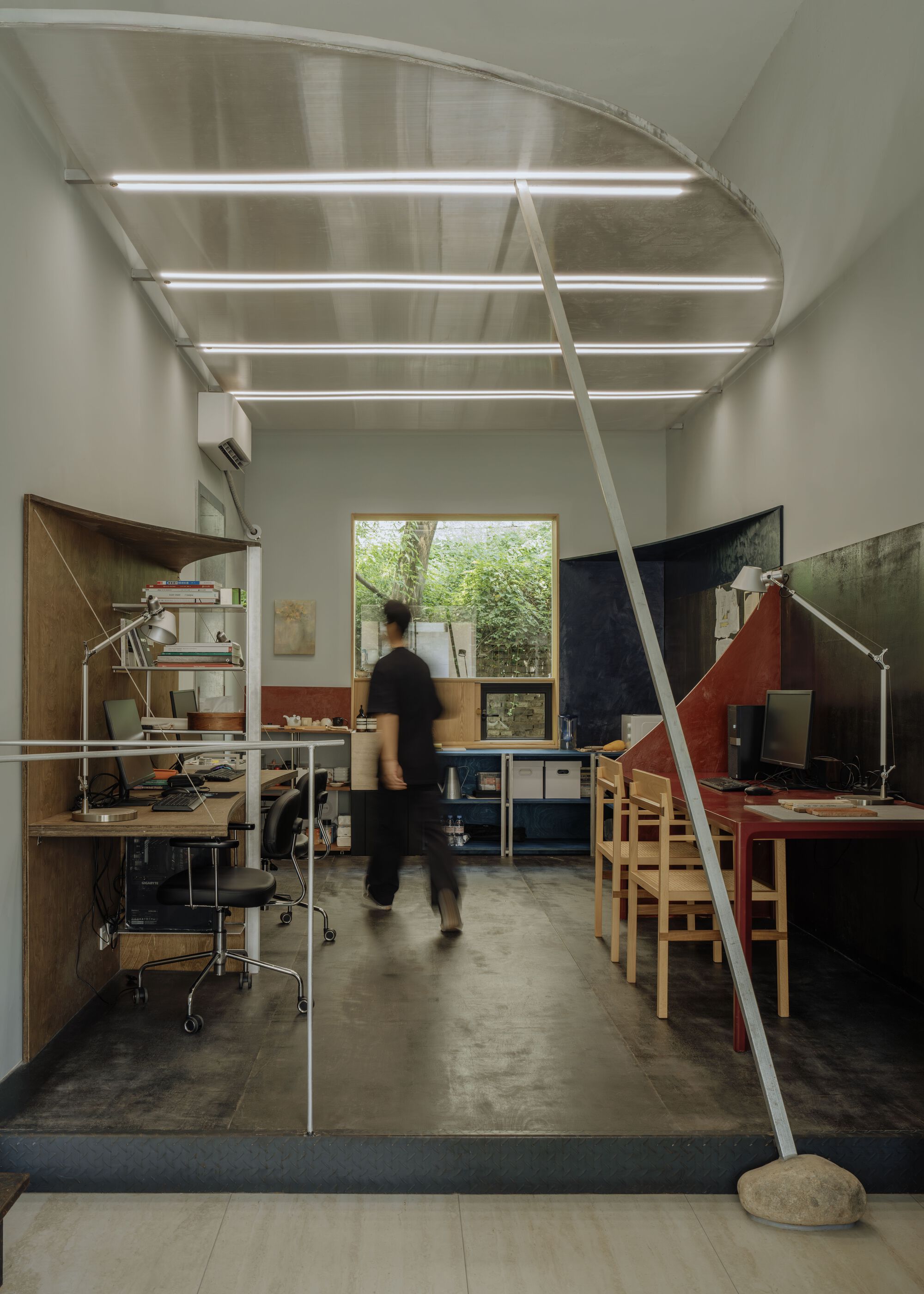 Studio workspace with vaulted steel ceiling and a person walking past workstations under linear lighting