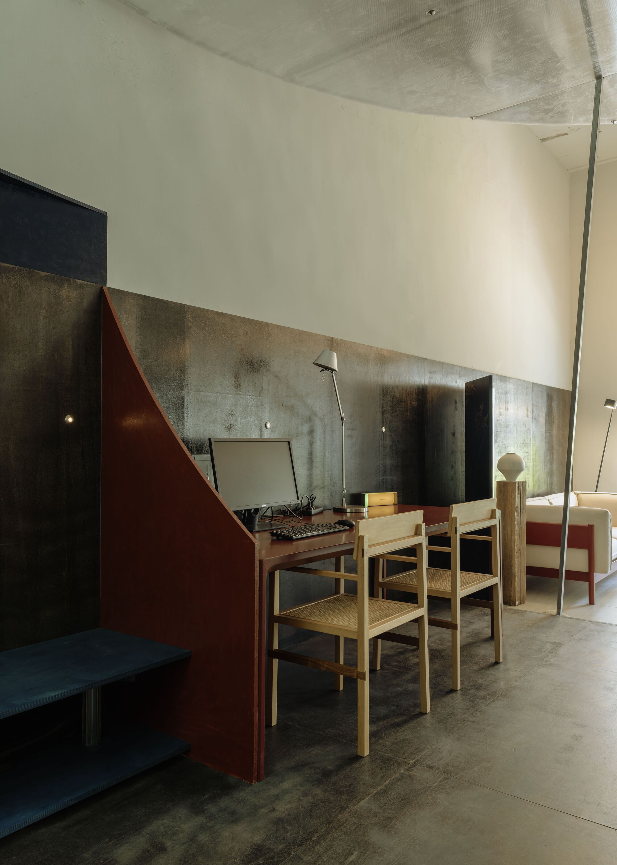 Dining area with timber chairs and maroon partition wall set against variegated metal panel backdrop