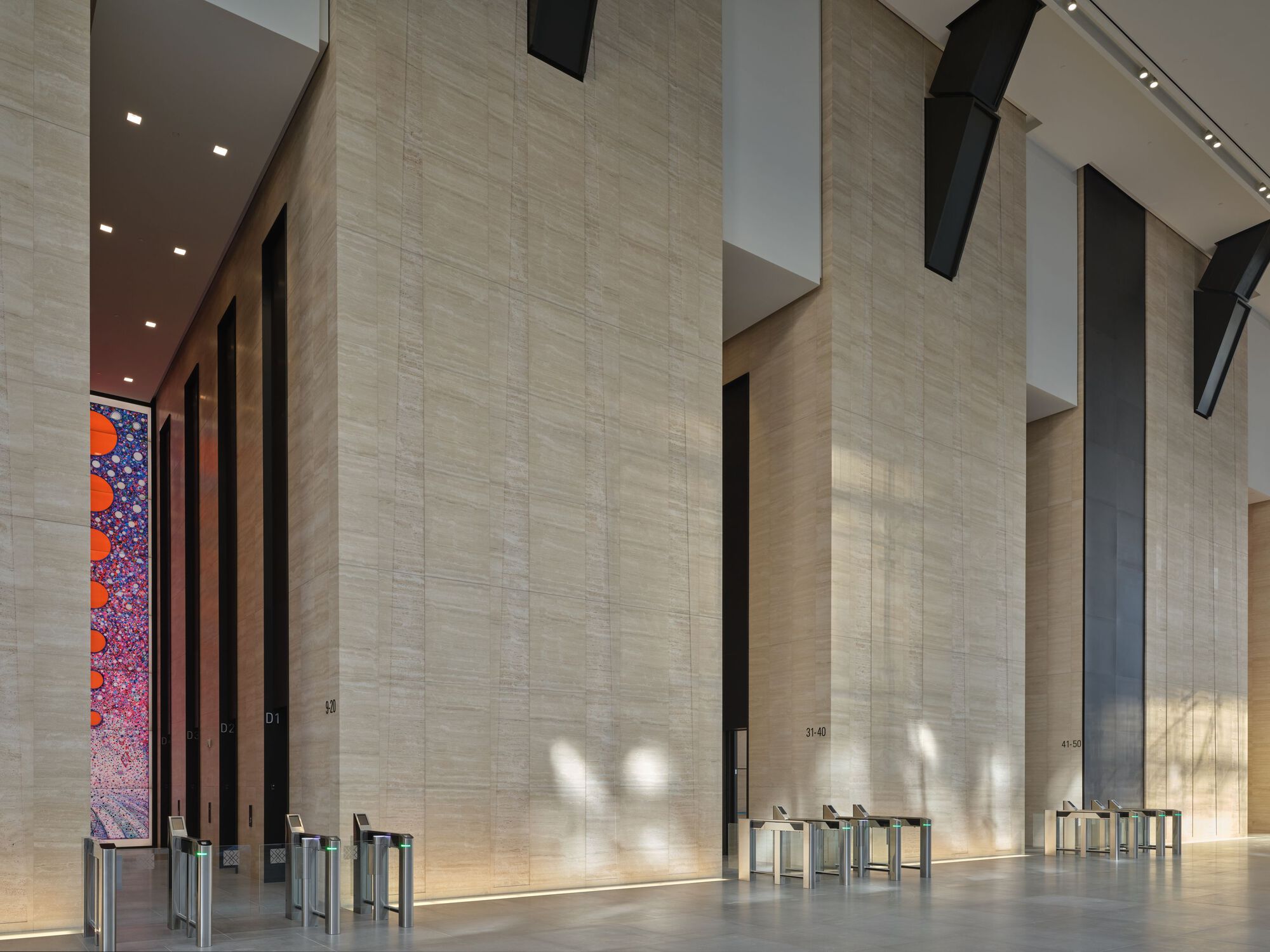 Double-height lobby with pale travertine walls and security turnstiles below suspended black ceiling elements