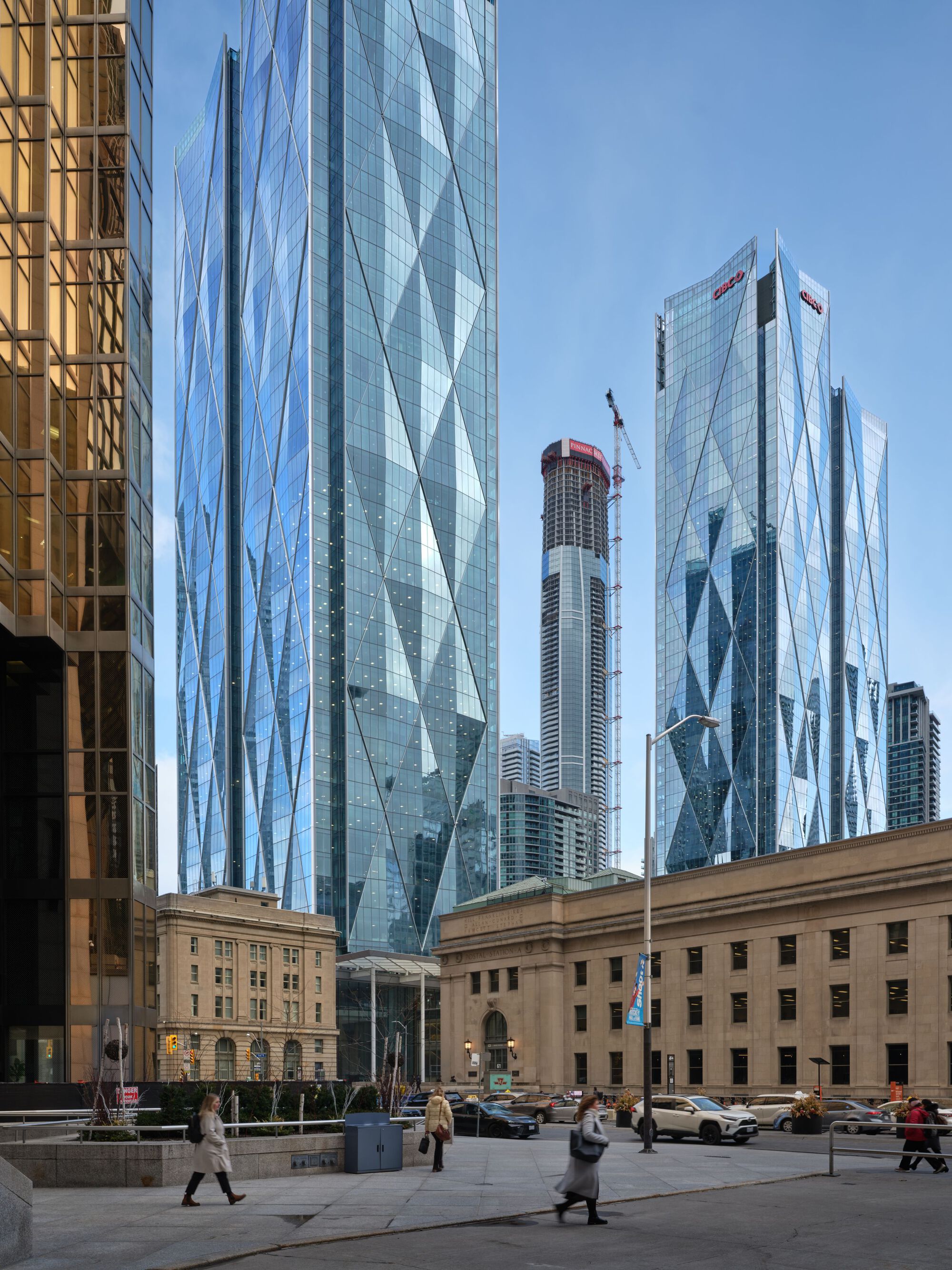 Street-level plaza with pedestrians crossing between heritage sandstone buildings and diagonal-braced glass towers