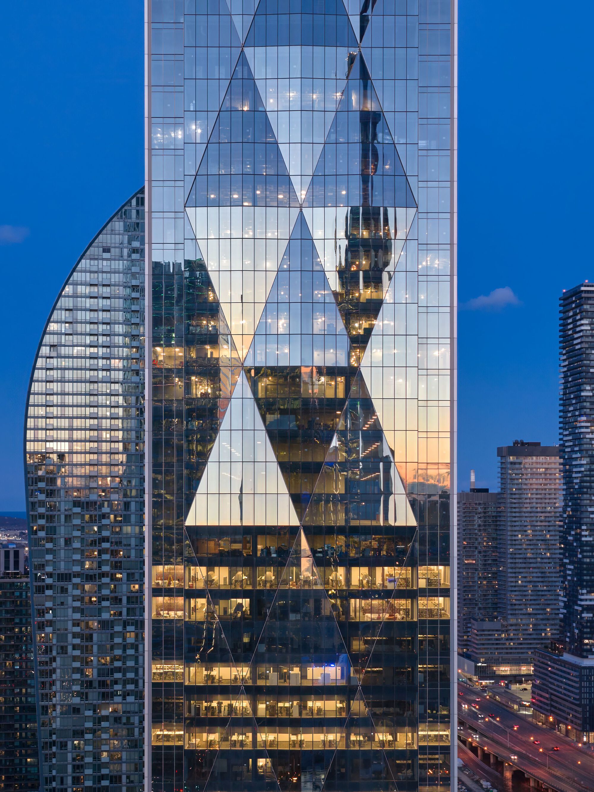 Close-up of glass facade with triangular structural bracing reflecting adjacent buildings at blue hour