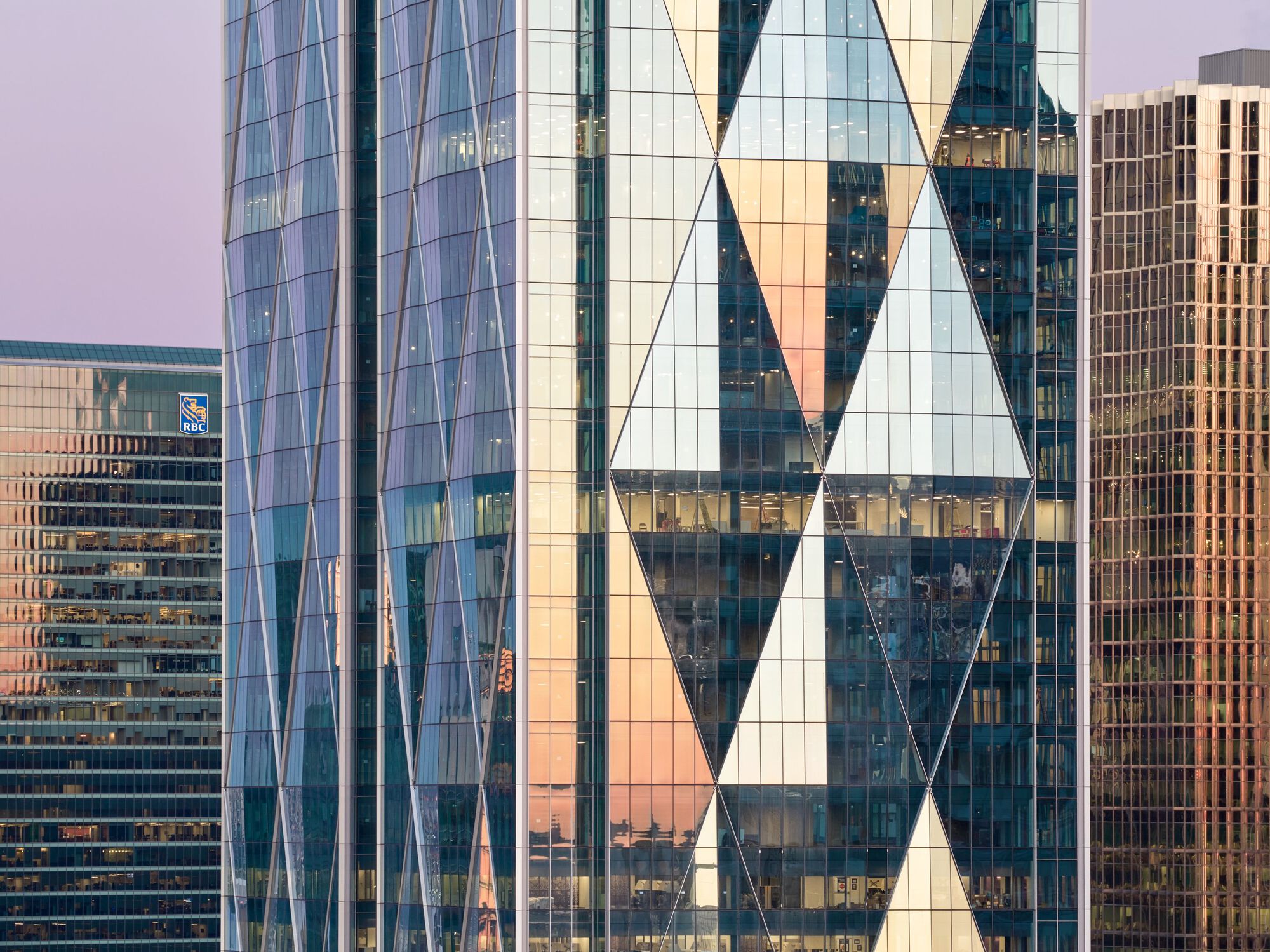 Detail of triangular glass panels and structural bracing against a pink sunset sky