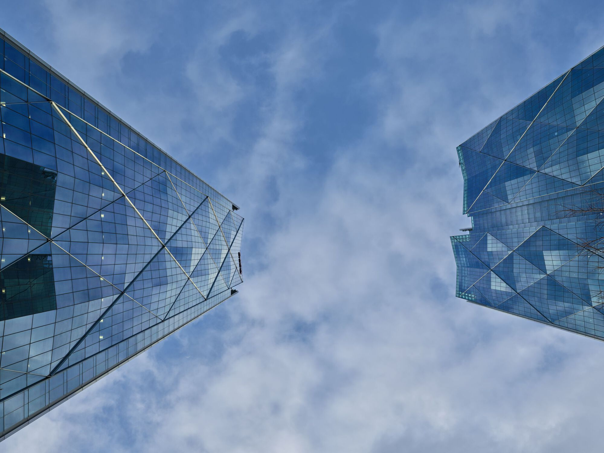 Upward view of the diagonal bracing on the glass curtain wall against a partly cloudy sky