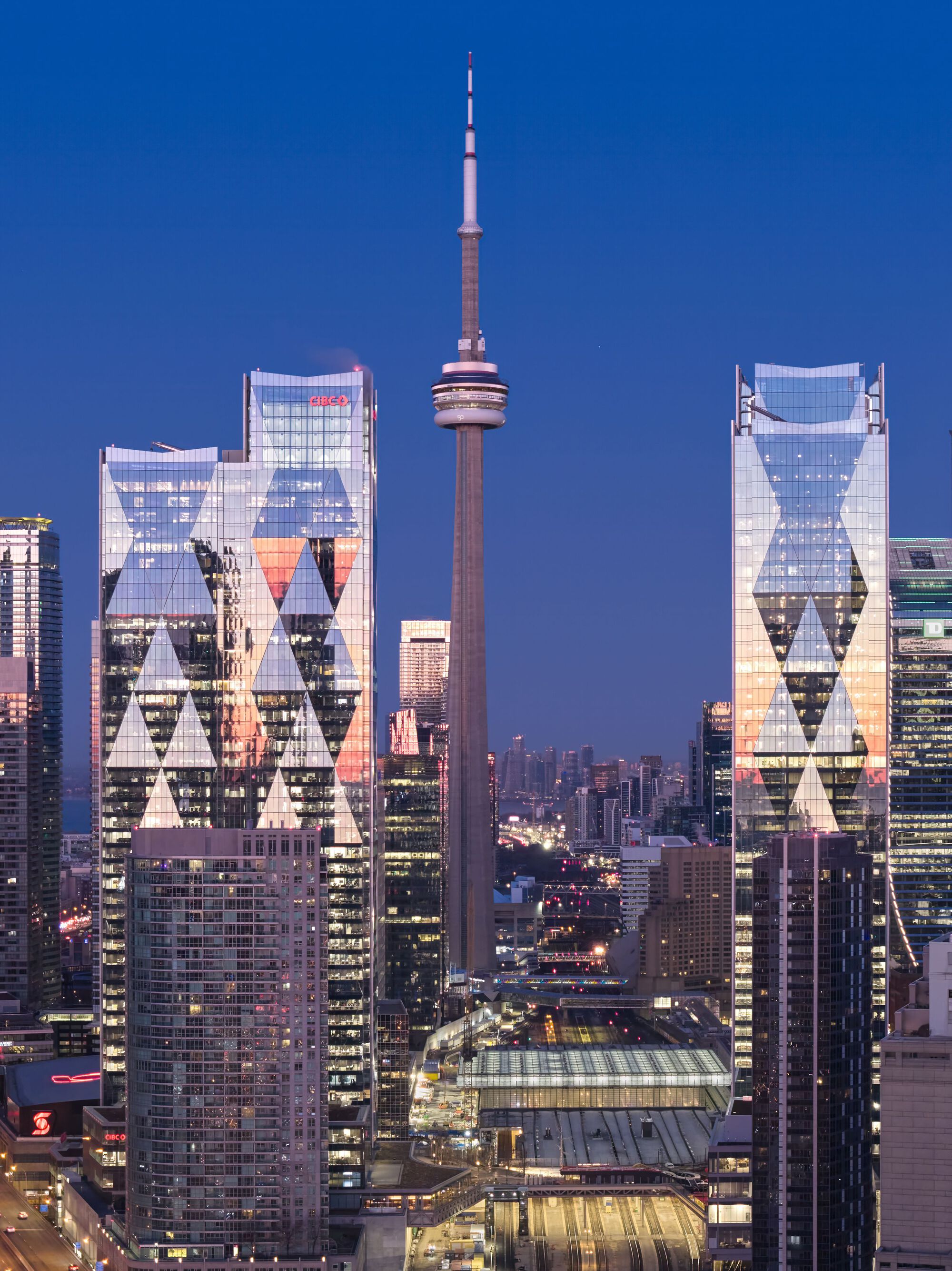 Twin glass towers with triangular window patterns illuminated against the deep blue evening sky