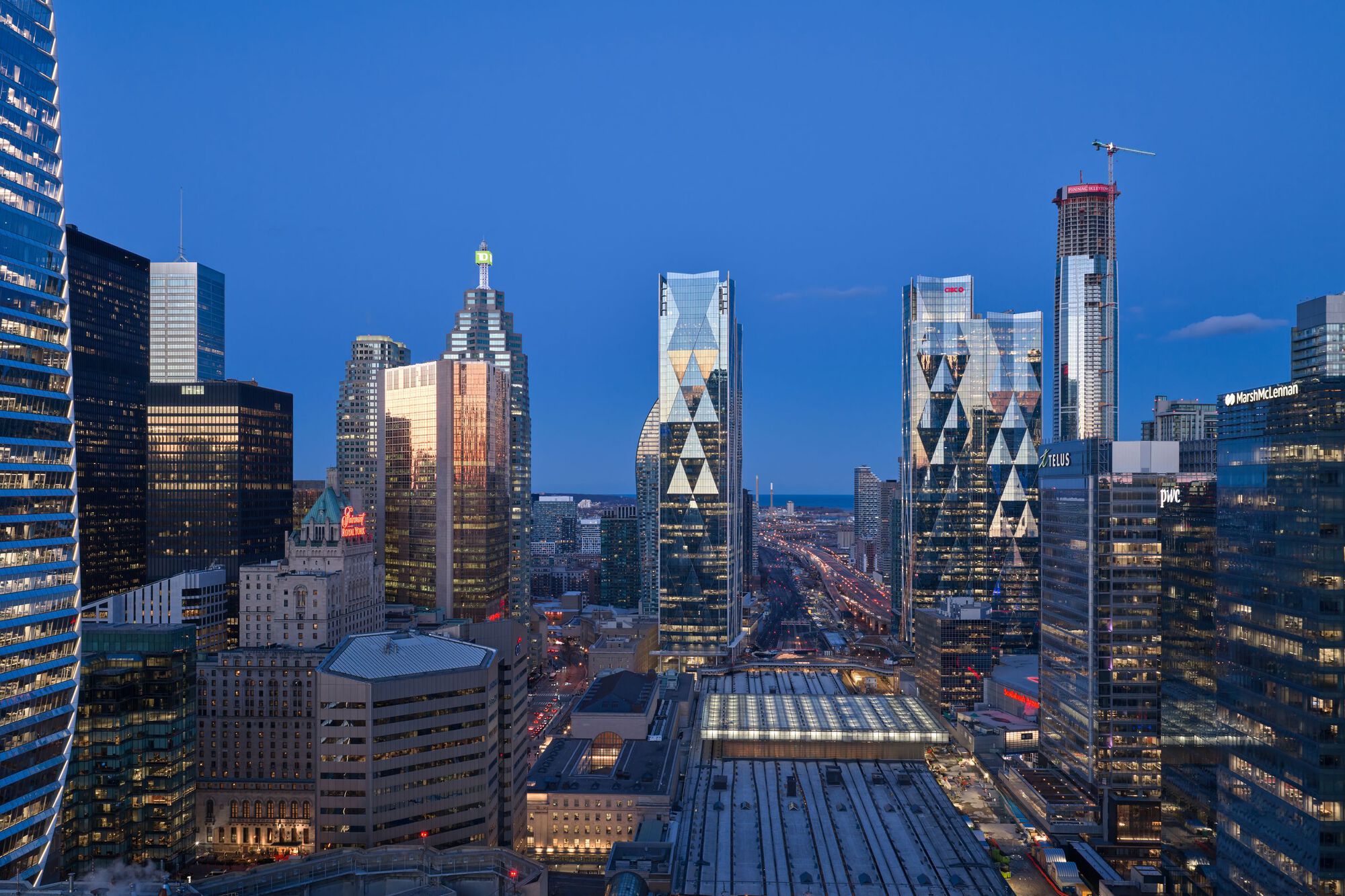 Skyline perspective with the paired towers and adjacent glass-roofed transit station at twilight