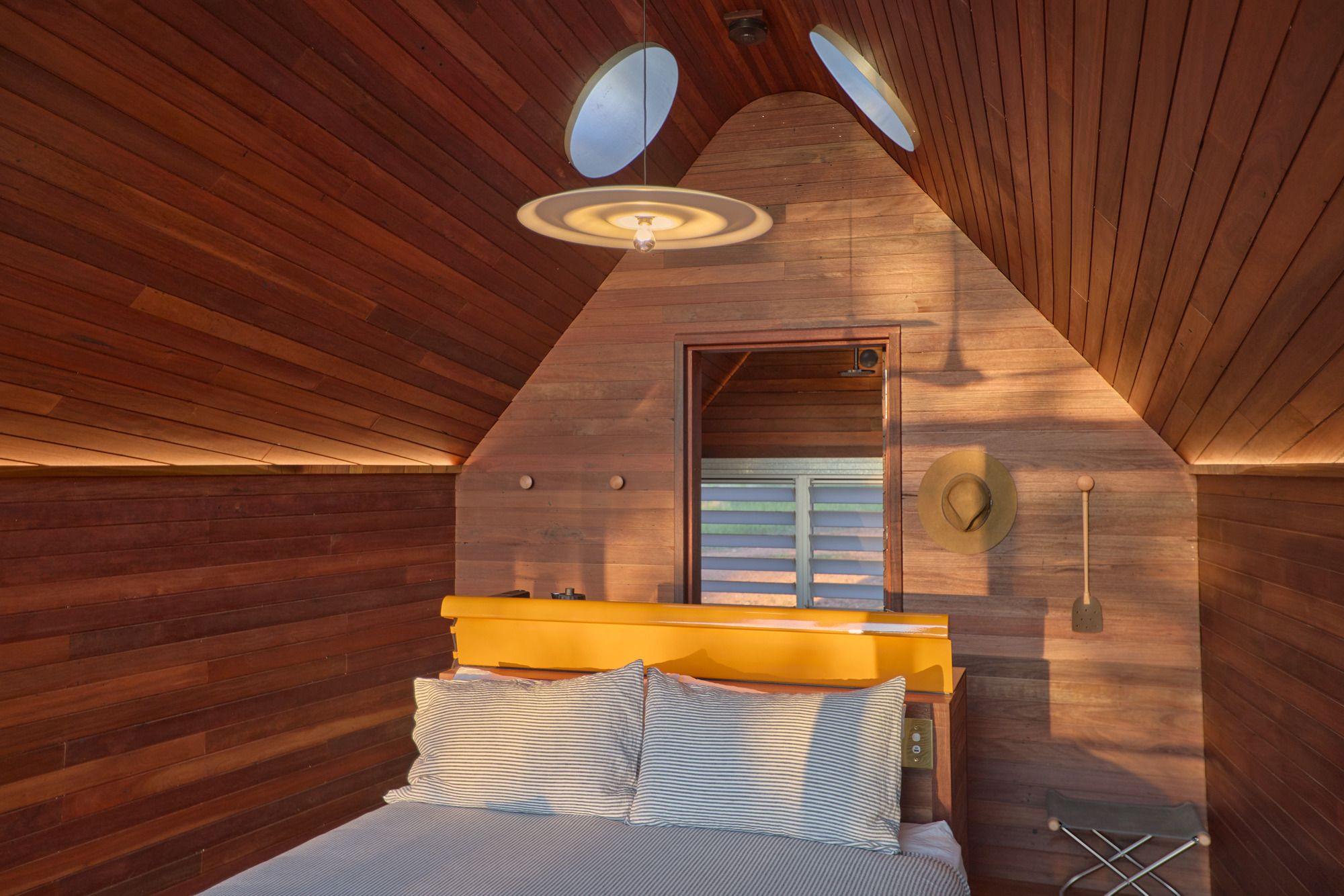 Interior view of wood-lined bedroom with angled ceiling and two circular skylights above the bed