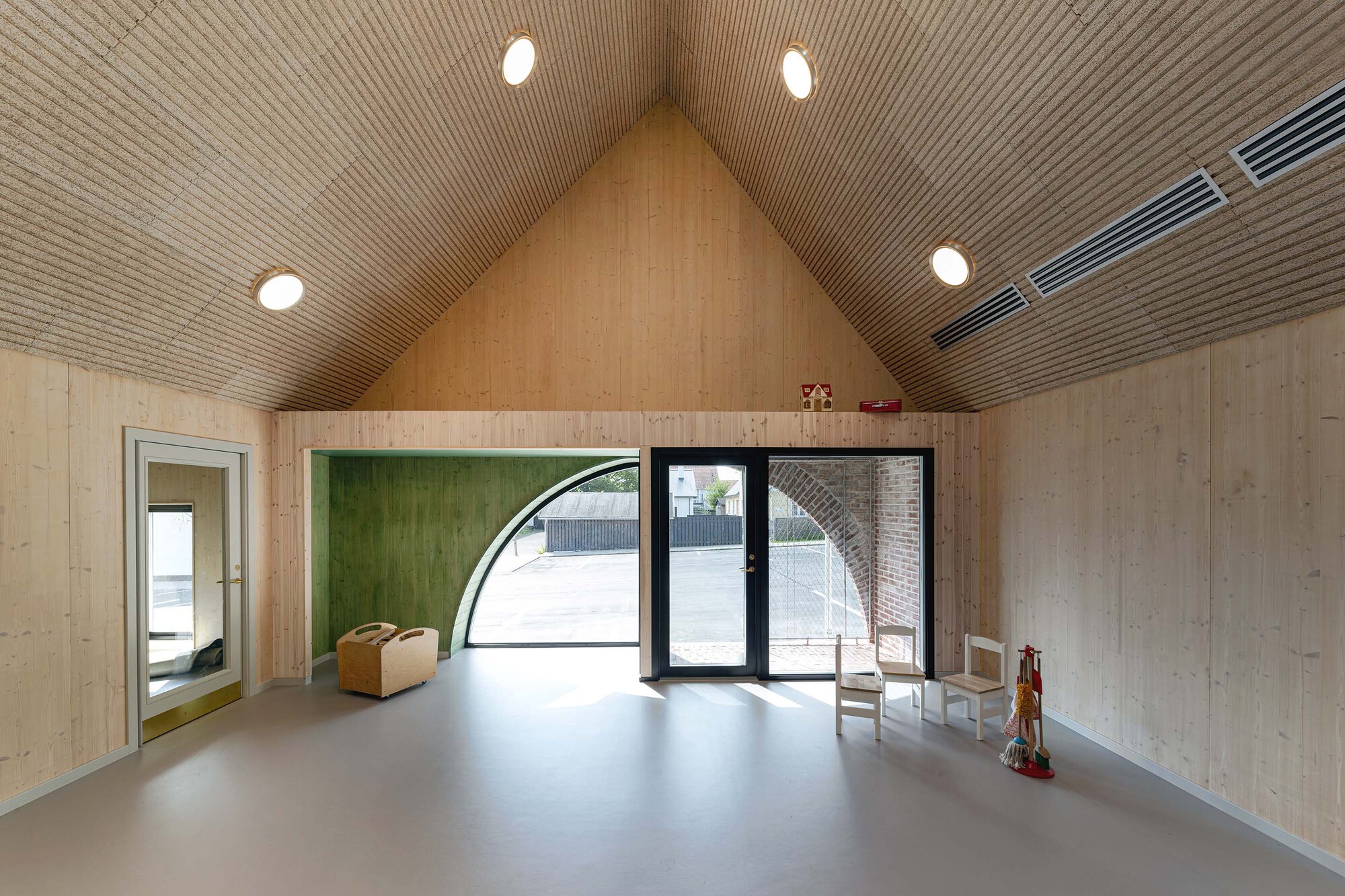Open room with pale timber walls, gabled ribbed ceiling and arched glazed door to courtyard