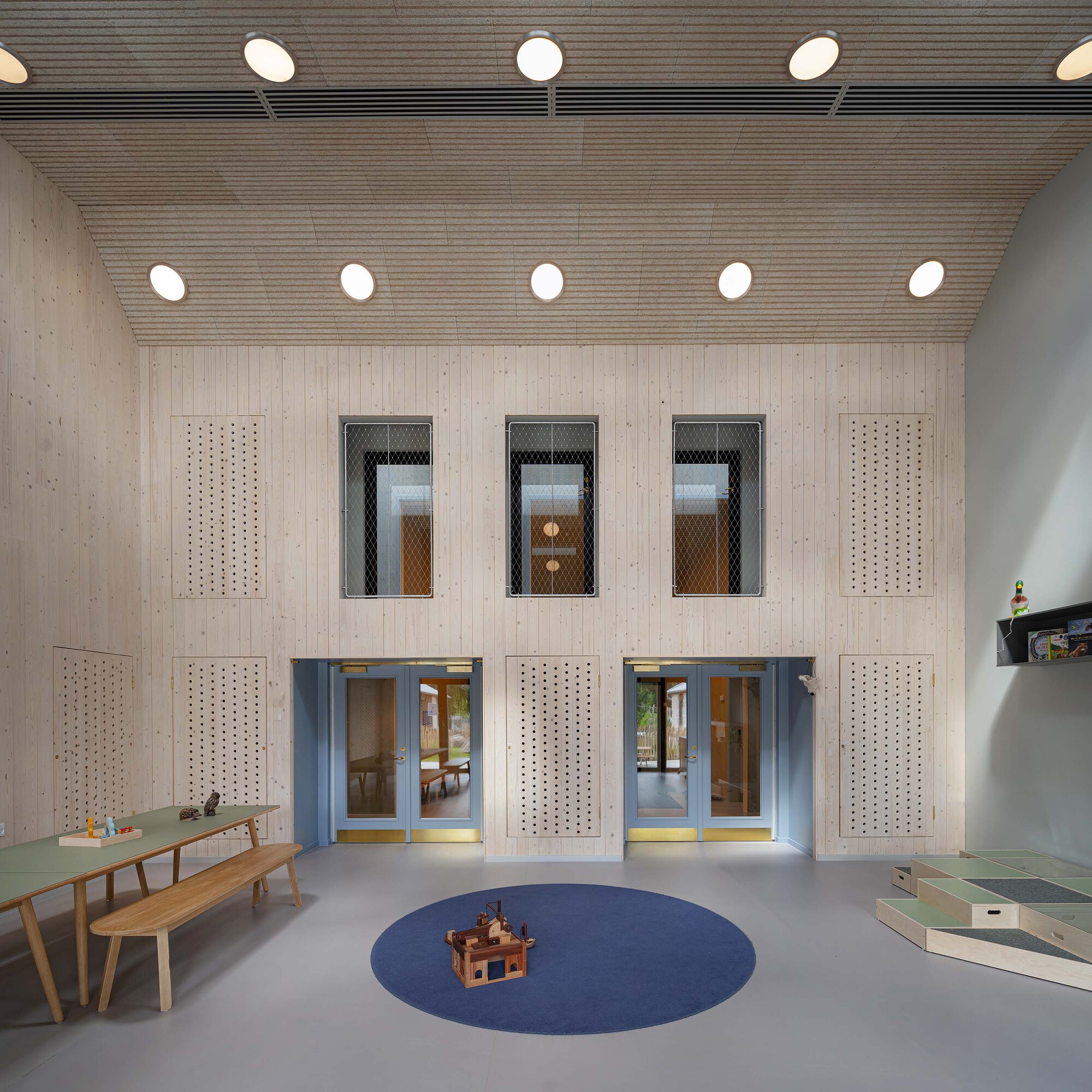 Double-height interior wall with perforated timber panels flanking three upper windows and two lower doorways