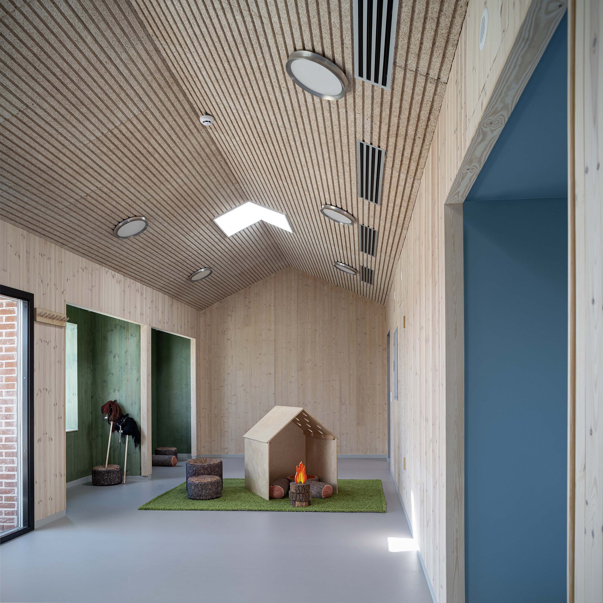 Corridor with ribbed timber ceiling, skylights and plywood play structure on artificial grass mat