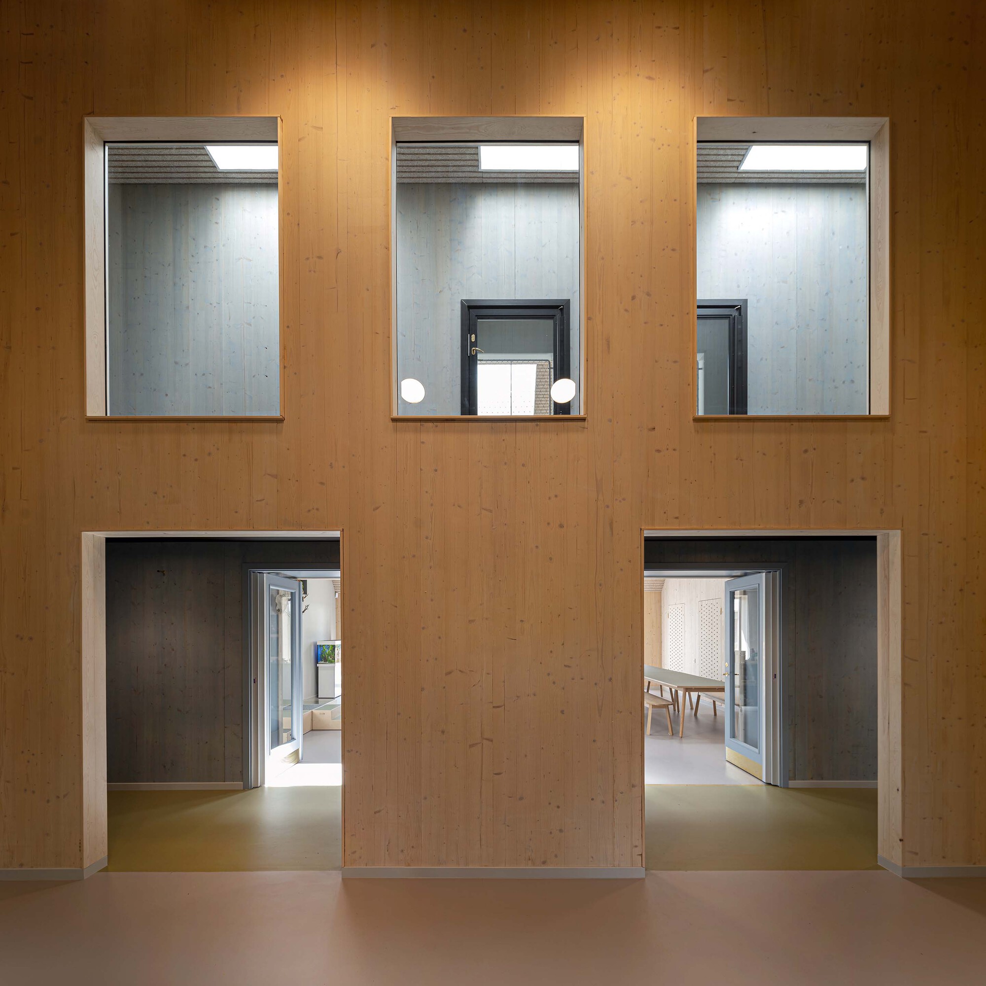 Plywood wall with three recessed windows above and two doorways opening to interior spaces