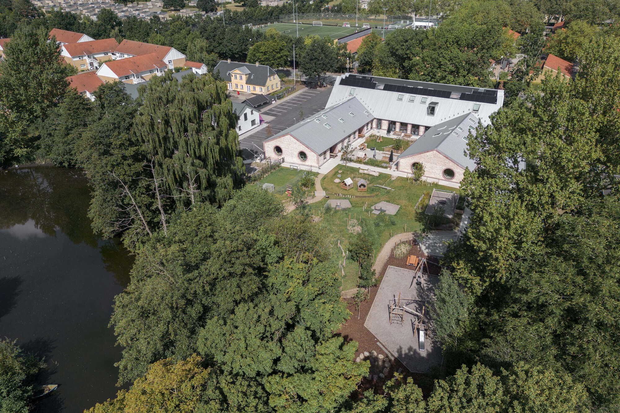 Aerial view of the gabled brick building with metal roof amid landscaped grounds and pond