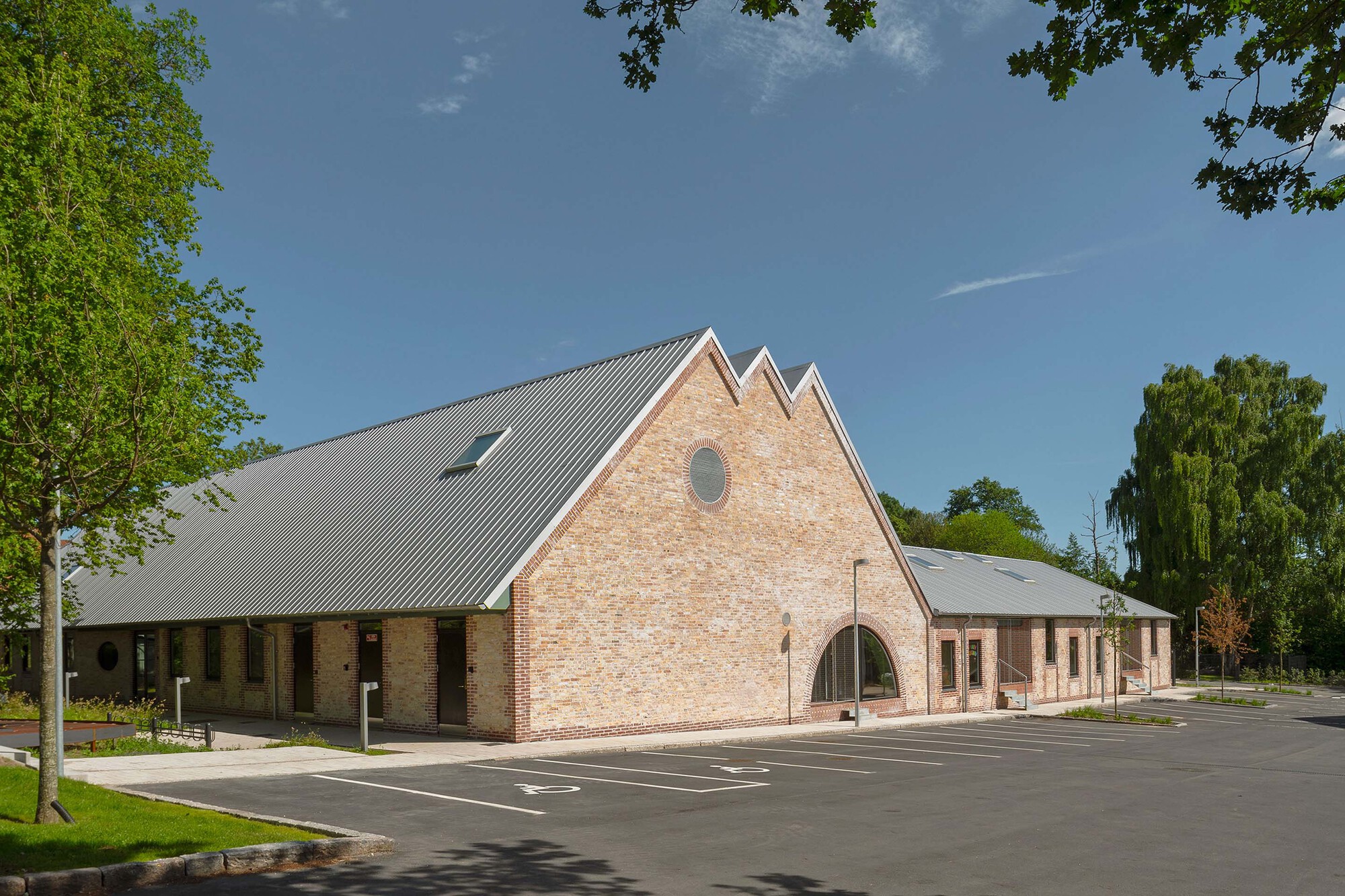 Street view of the triple-gabled brick facade with metal roof and parking area on a clear day
