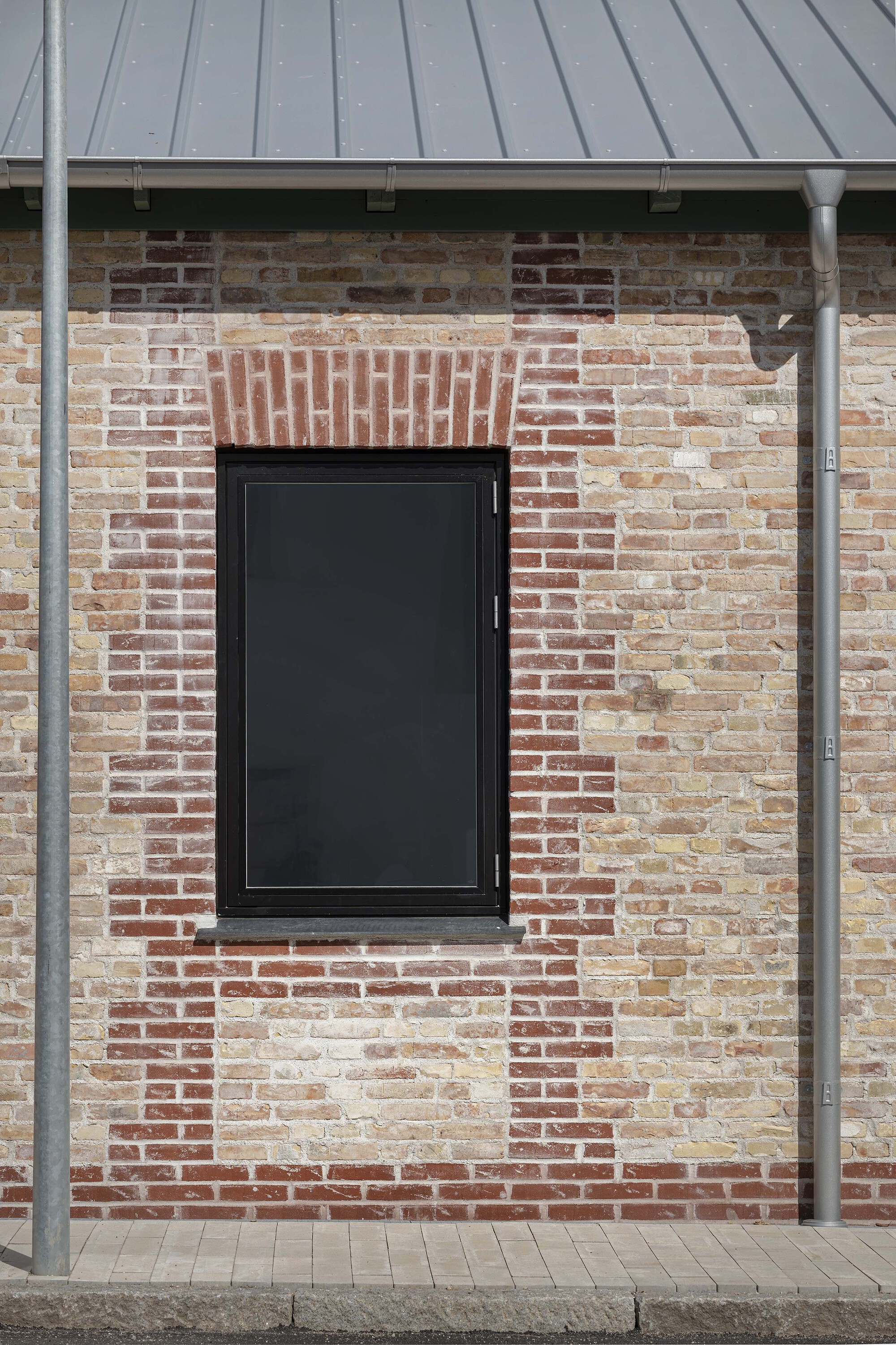 Black-framed window set in reclaimed brick wall with decorative brickwork header beneath a metal overhang