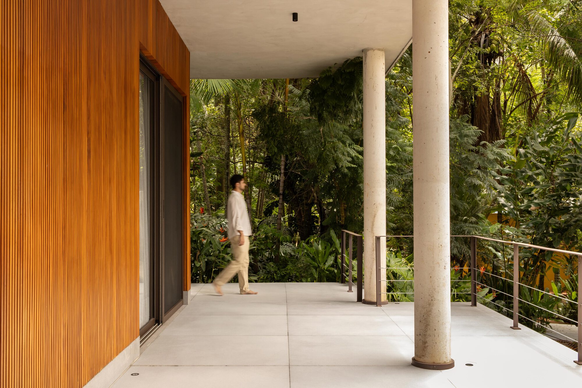 Covered terrace with large-format concrete pavers and cylindrical columns as person walks past timber-clad wall