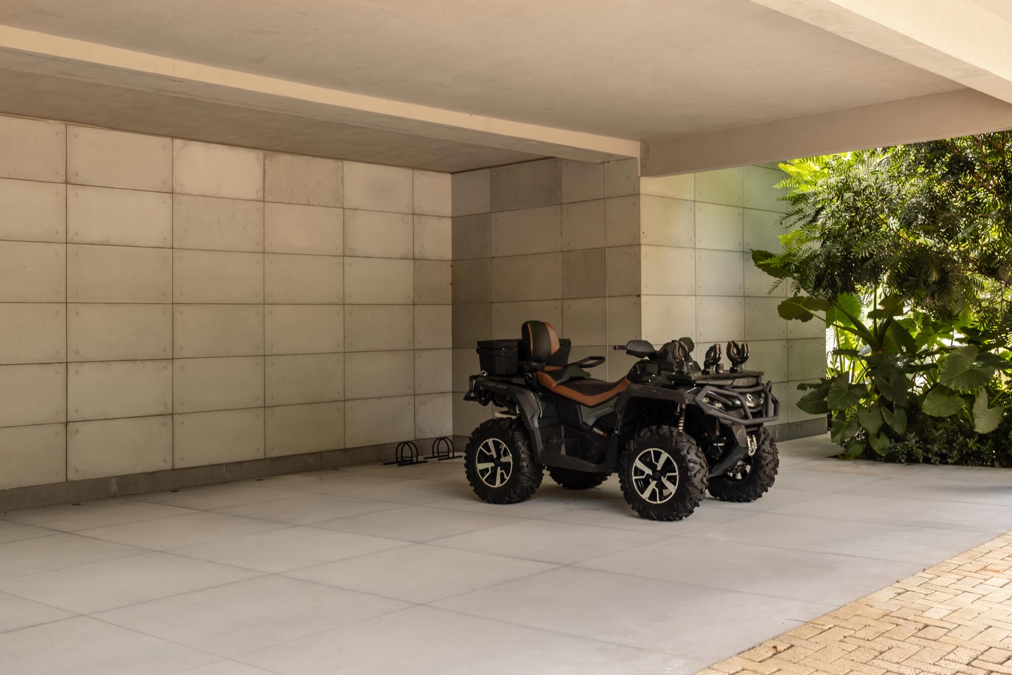 Carport with square concrete tile wall and all-terrain vehicle parked beside paved driveway