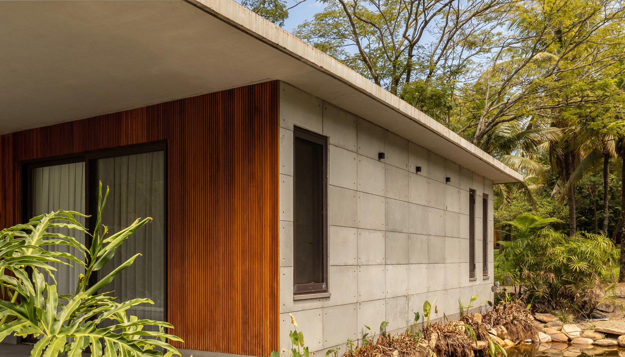 Facade combining vertical timber cladding and concrete panels under a flat roof with garden plantings
