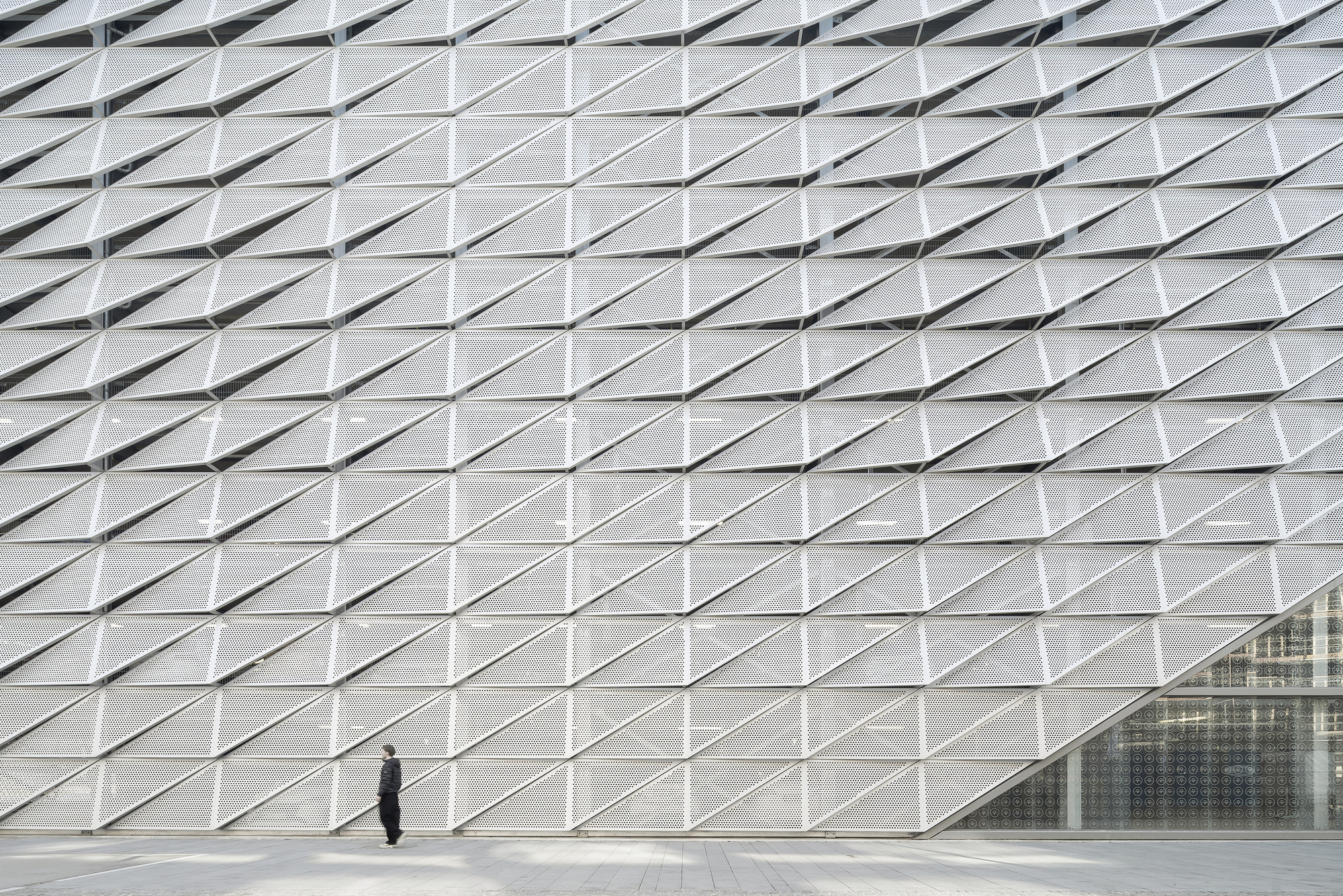 Facade wall of repeating triangular metal panels with a pedestrian standing near the glazed entrance