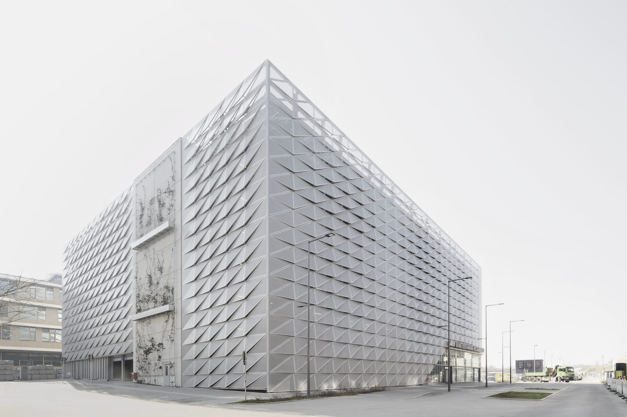 Rear elevation showing the faceted metal envelope and exposed concrete stair tower under grey skies