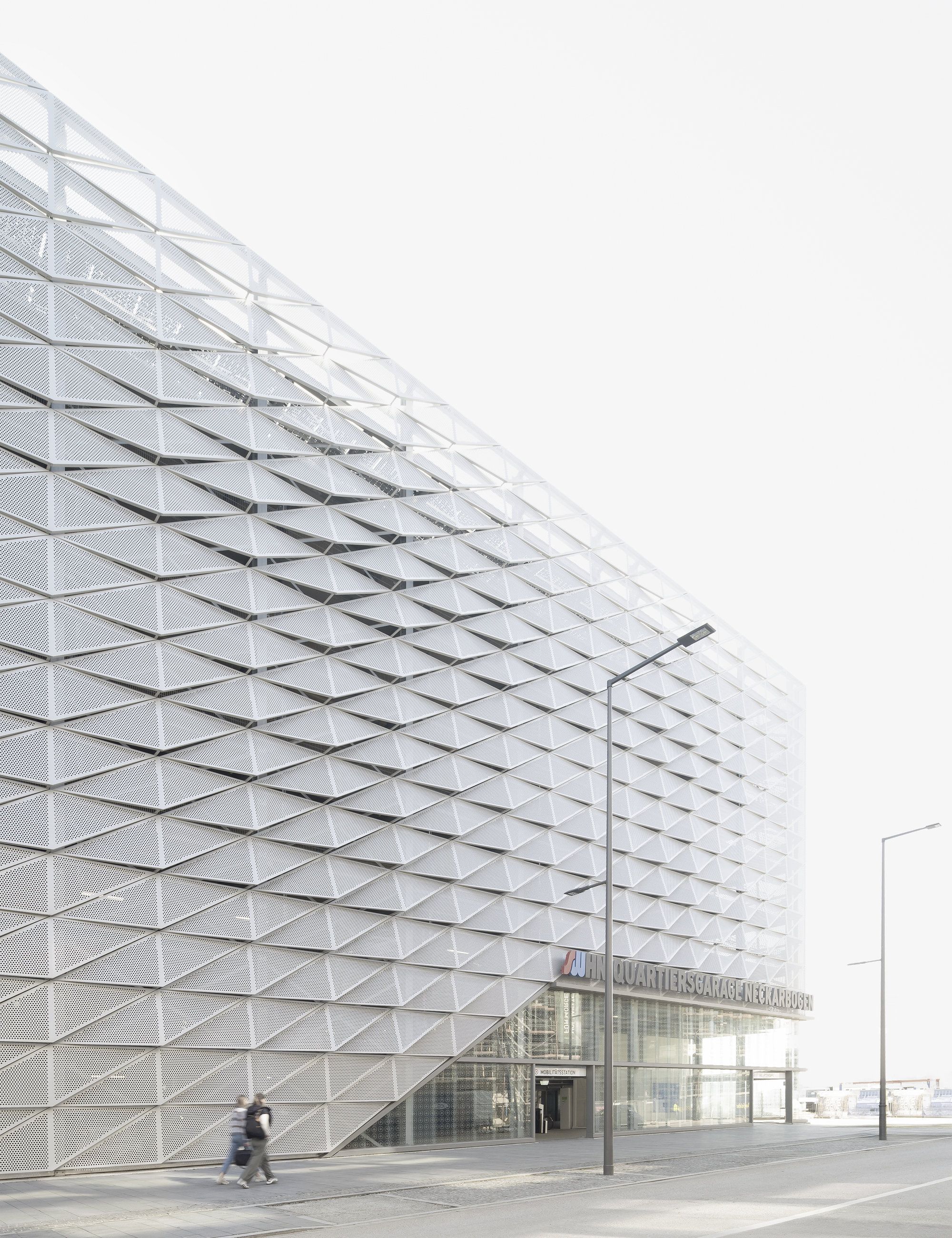 Triangulated metal facade with embedded glass panels at street level with a person walking past