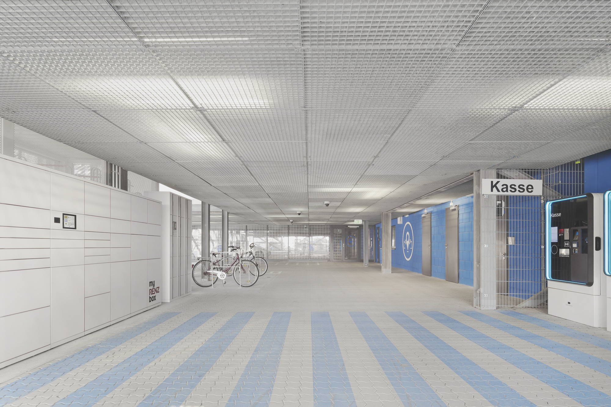 Interior ground level entry hall with metal mesh ceiling and striped pavers leading to bicycle parking