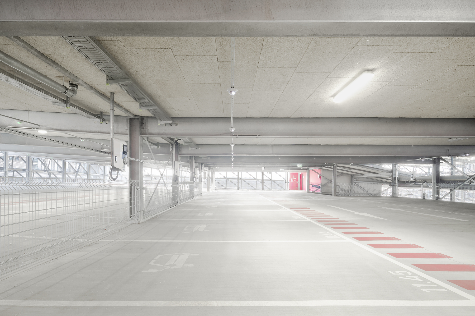 Upper parking level with exposed concrete ceiling beams and metal perimeter screen filtering daylight
