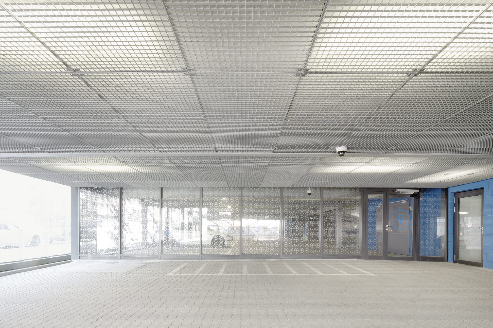 Parking deck interior showing metal mesh ceiling and patterned glass screen with bicycles visible outside