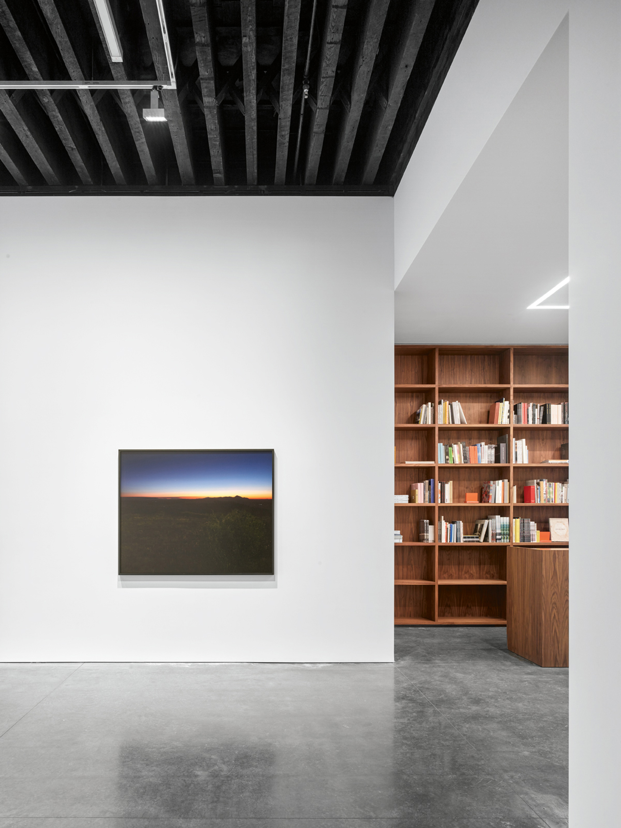 White-walled room with exposed dark ceiling joists and timber bookshelf visible through opening