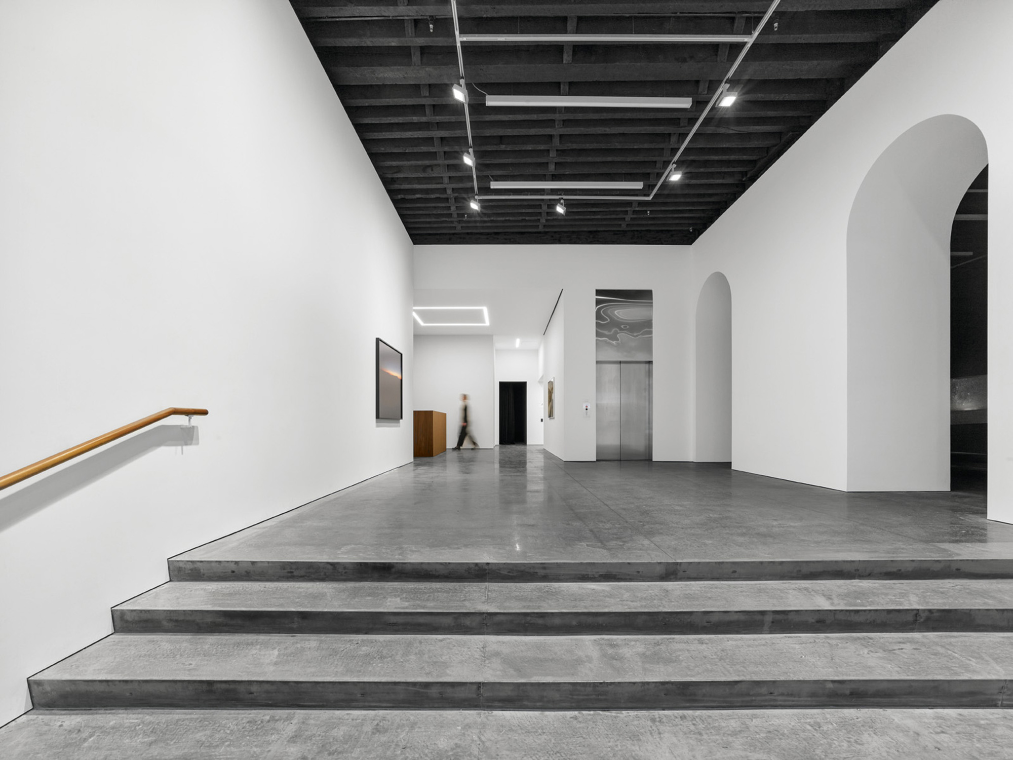Wide concrete stairs with timber handrail leading to gallery space with arched doorways