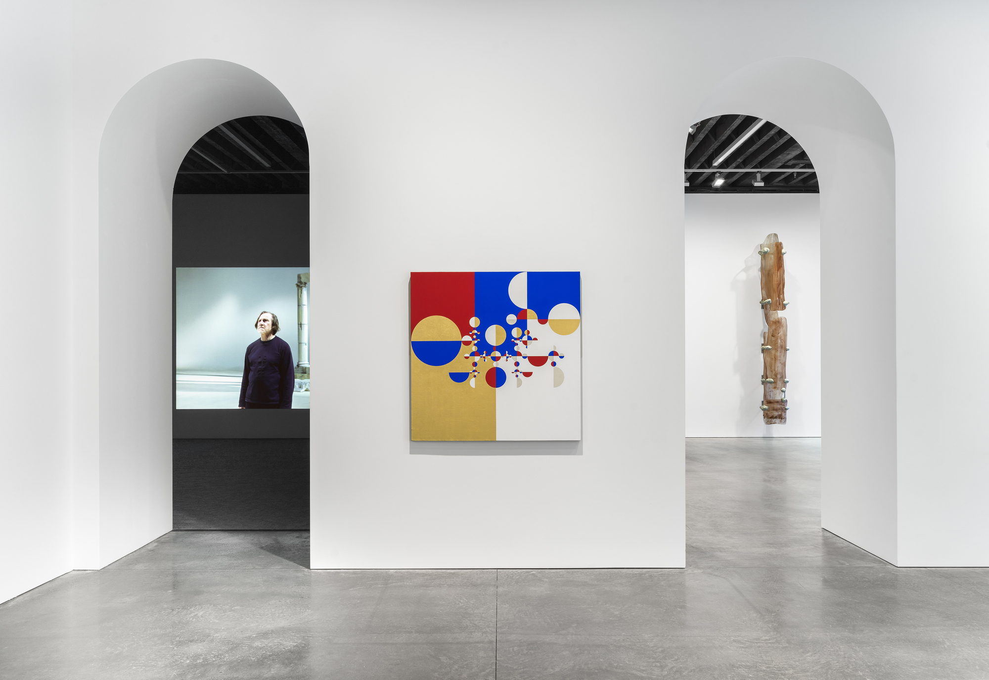 White gallery wall with paired arched openings and concrete floor displaying artwork between them