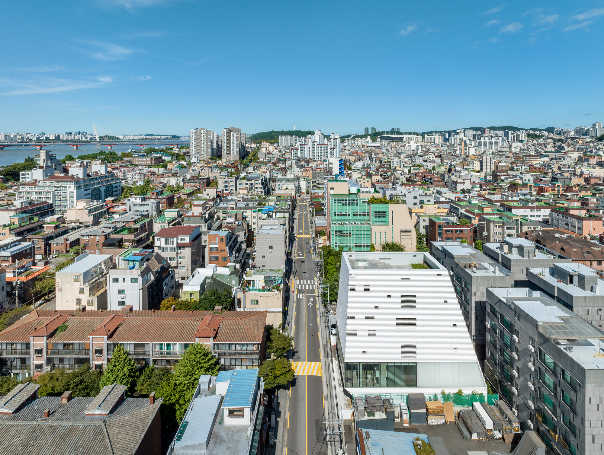 Aerial view of the white rectilinear volume among surrounding residential blocks and waterfront beyond