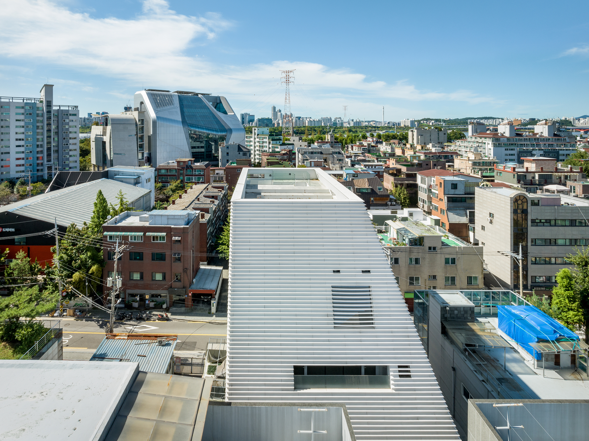 Elevated view of the horizontal louver roof extending across the dense neighborhood under summer sky