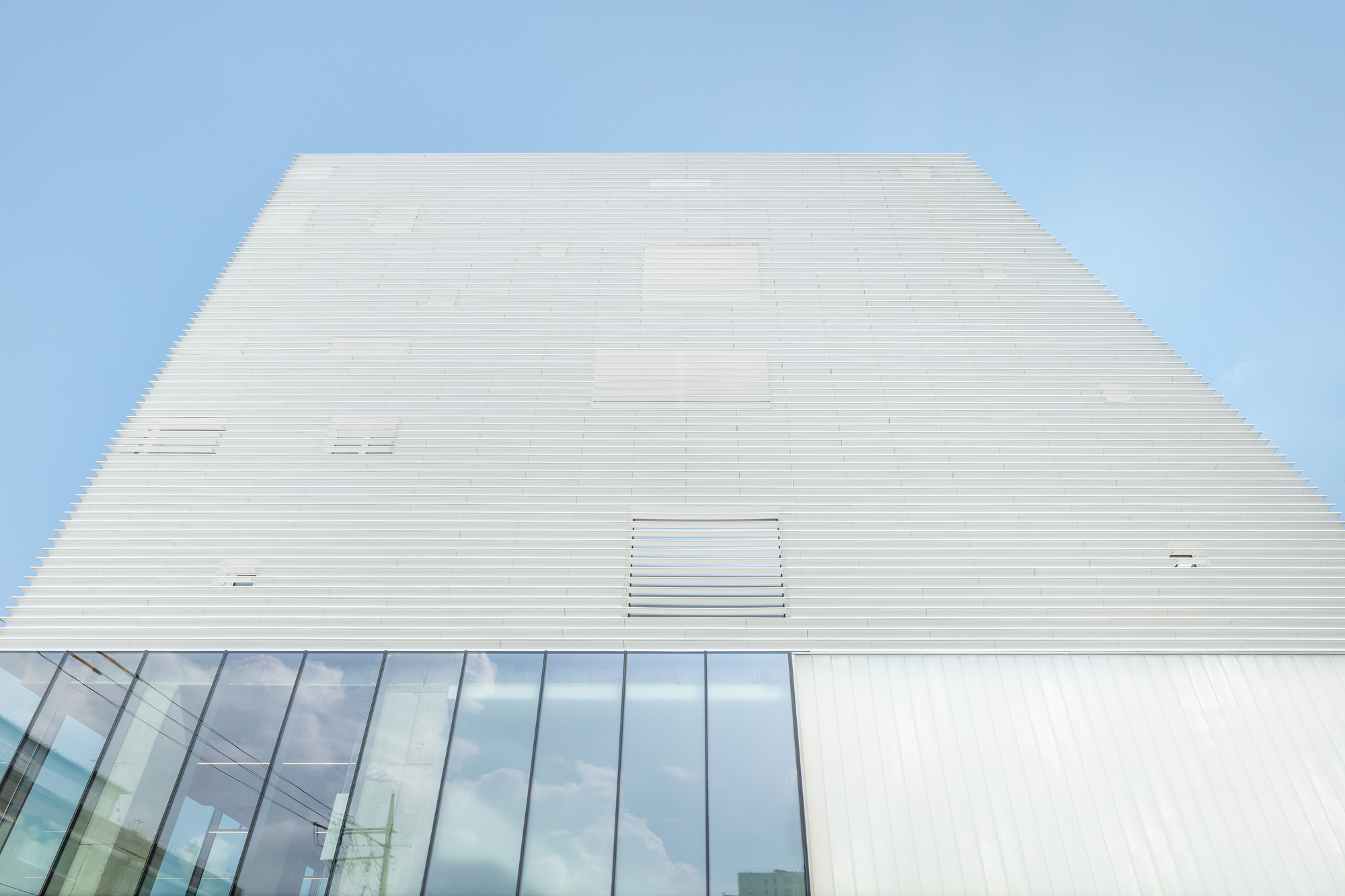 Upward view of the ribbed white facade tapering against a clear blue sky