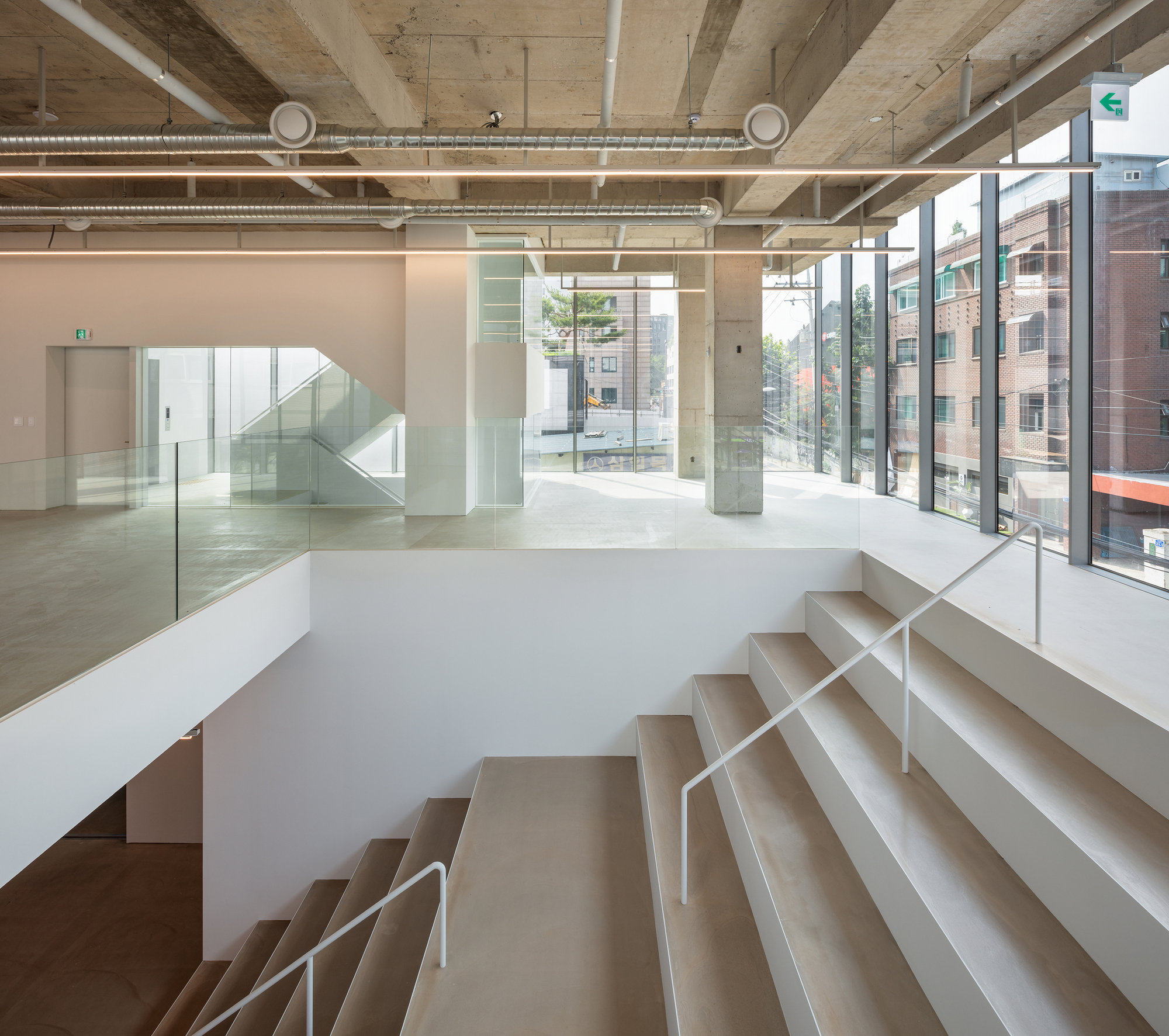 Interior split-level staircase with glass railings and exposed concrete ceiling under natural daylight