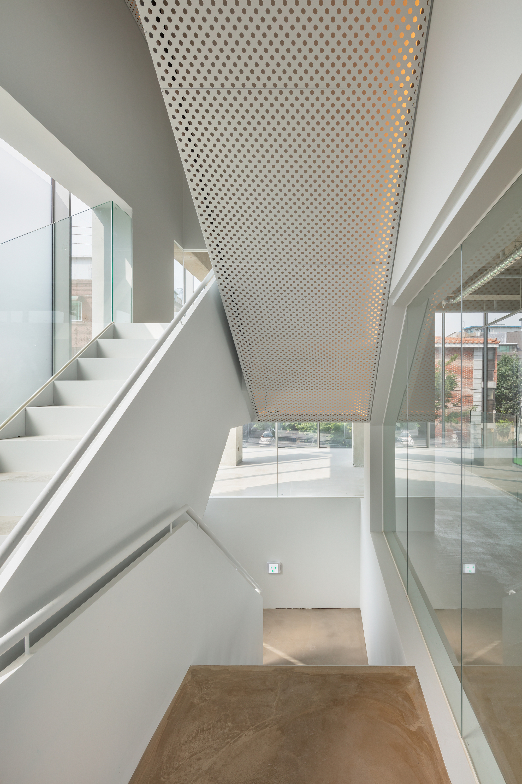 Stair landing with angled perforated metal ceiling and glass walls overlooking adjacent spaces