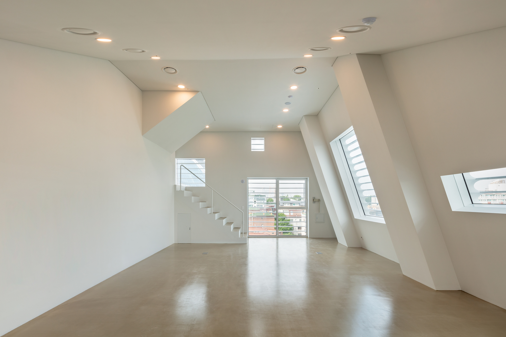 Gallery space with sloped white walls and angled skylights casting shadows on polished concrete floor