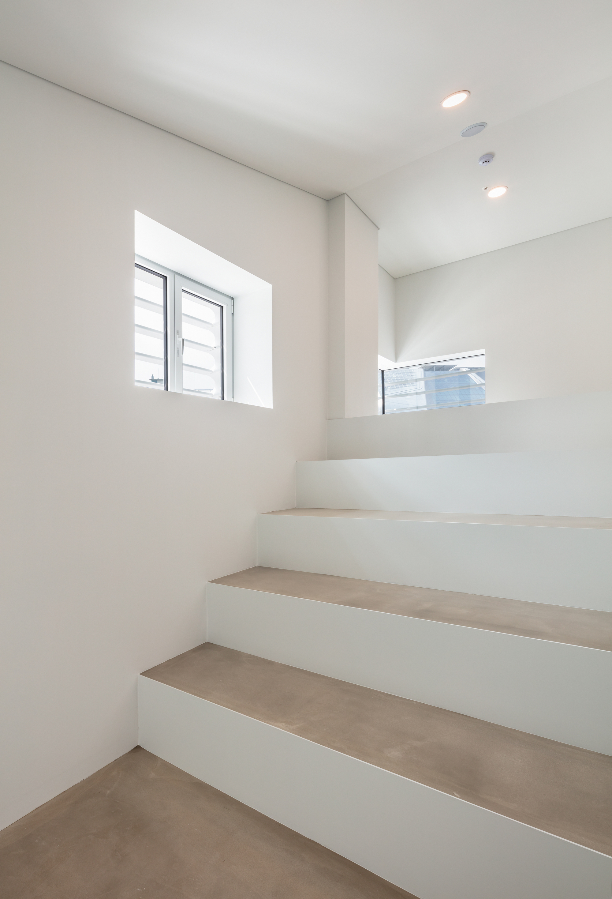 White-painted staircase with light wood treads ascending past two deep-set windows with natural daylight