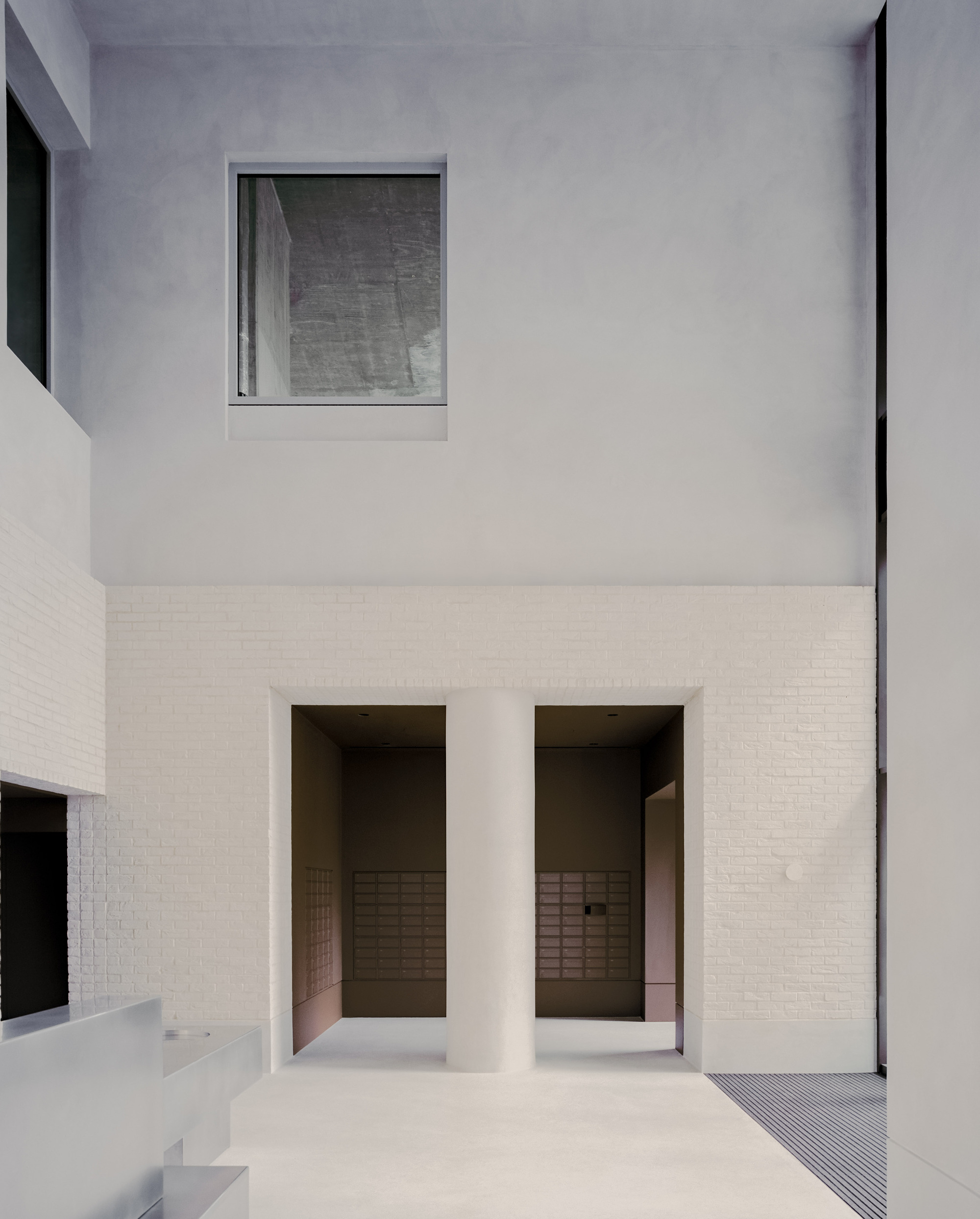 Courtyard view showing two deep-set openings in a white brick base beneath rendered upper walls