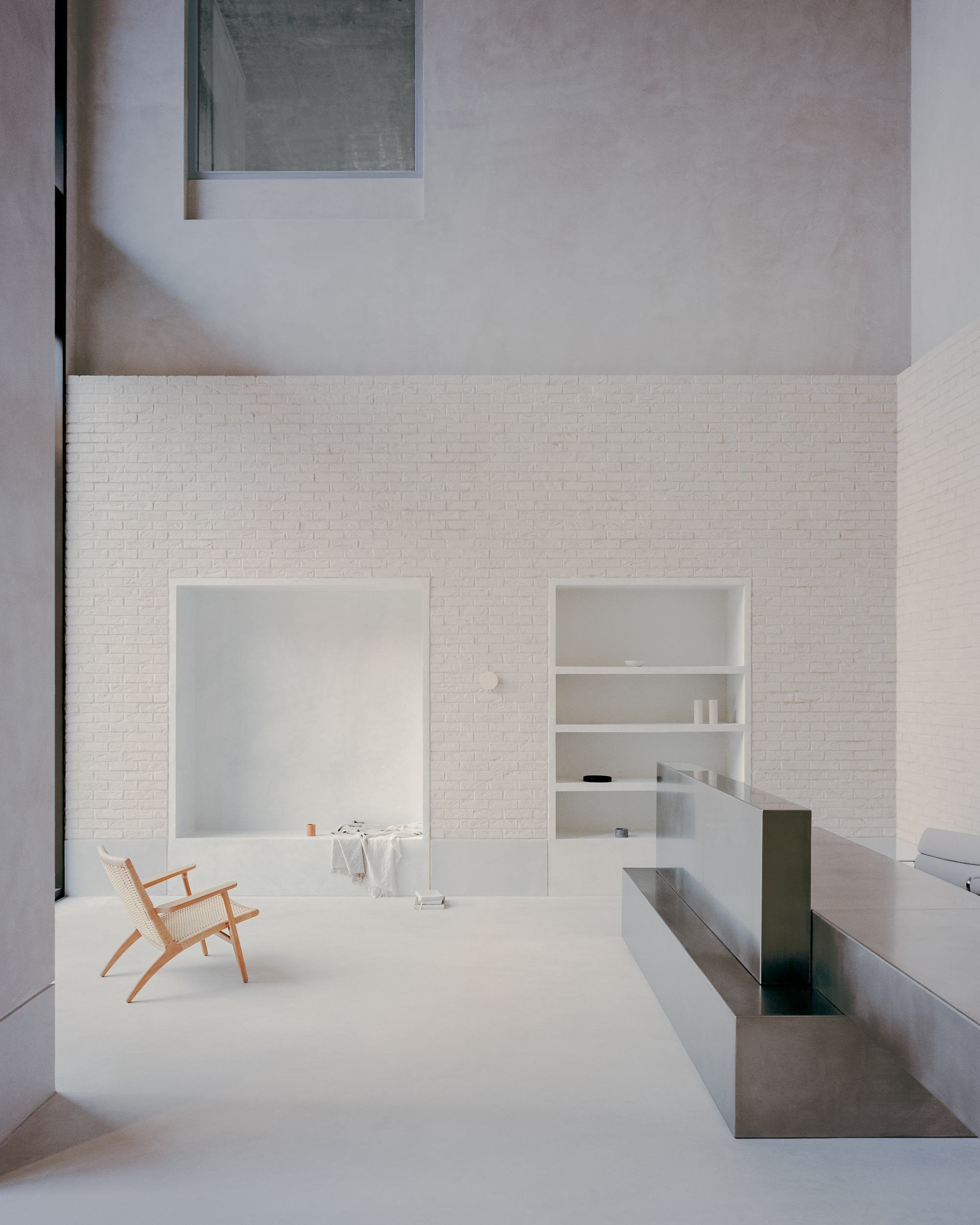Double-height courtyard with white brick walls and a timber chair on pale flooring