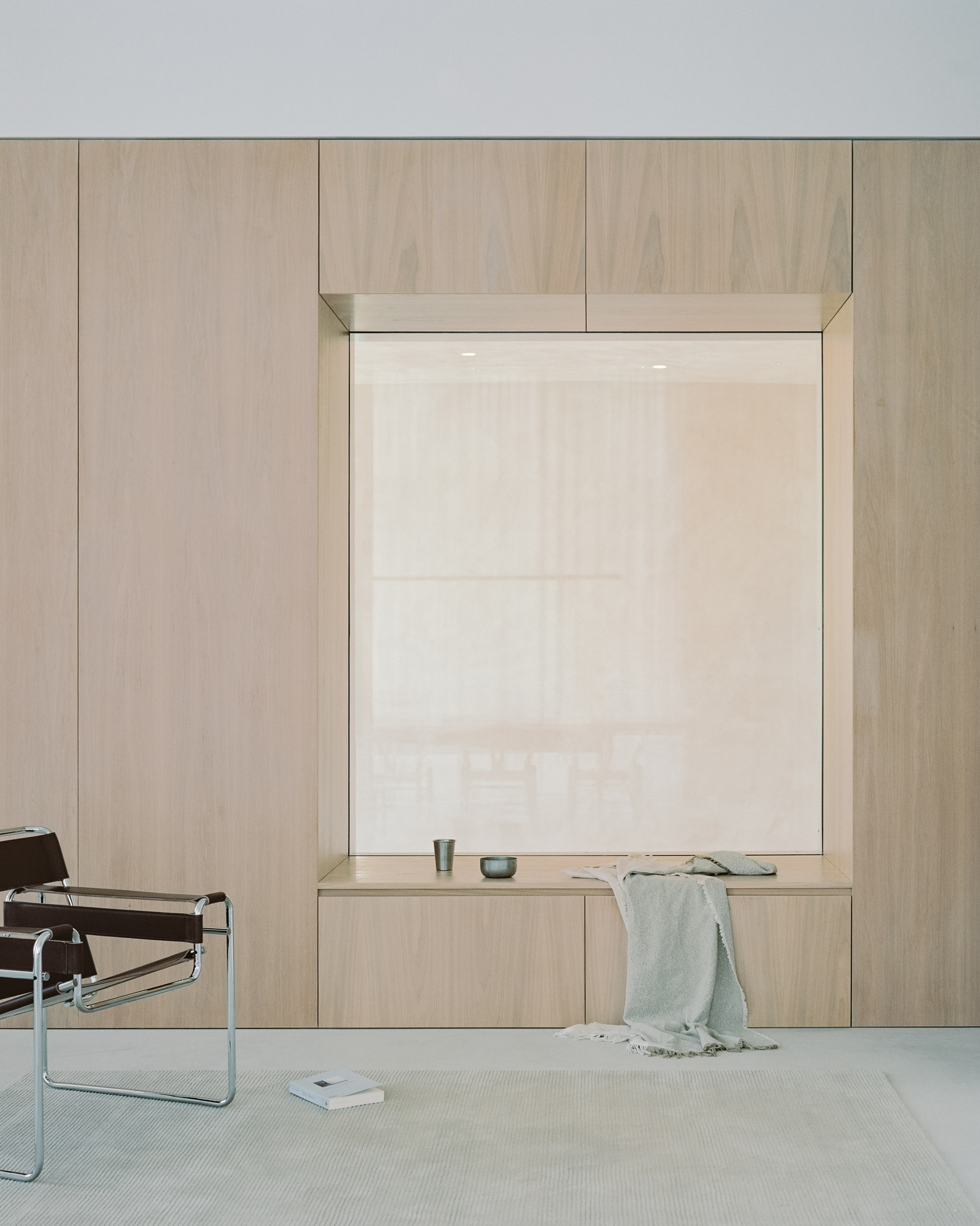 Timber-framed window alcove with built-in bench and sheer white roller shade in pale interior