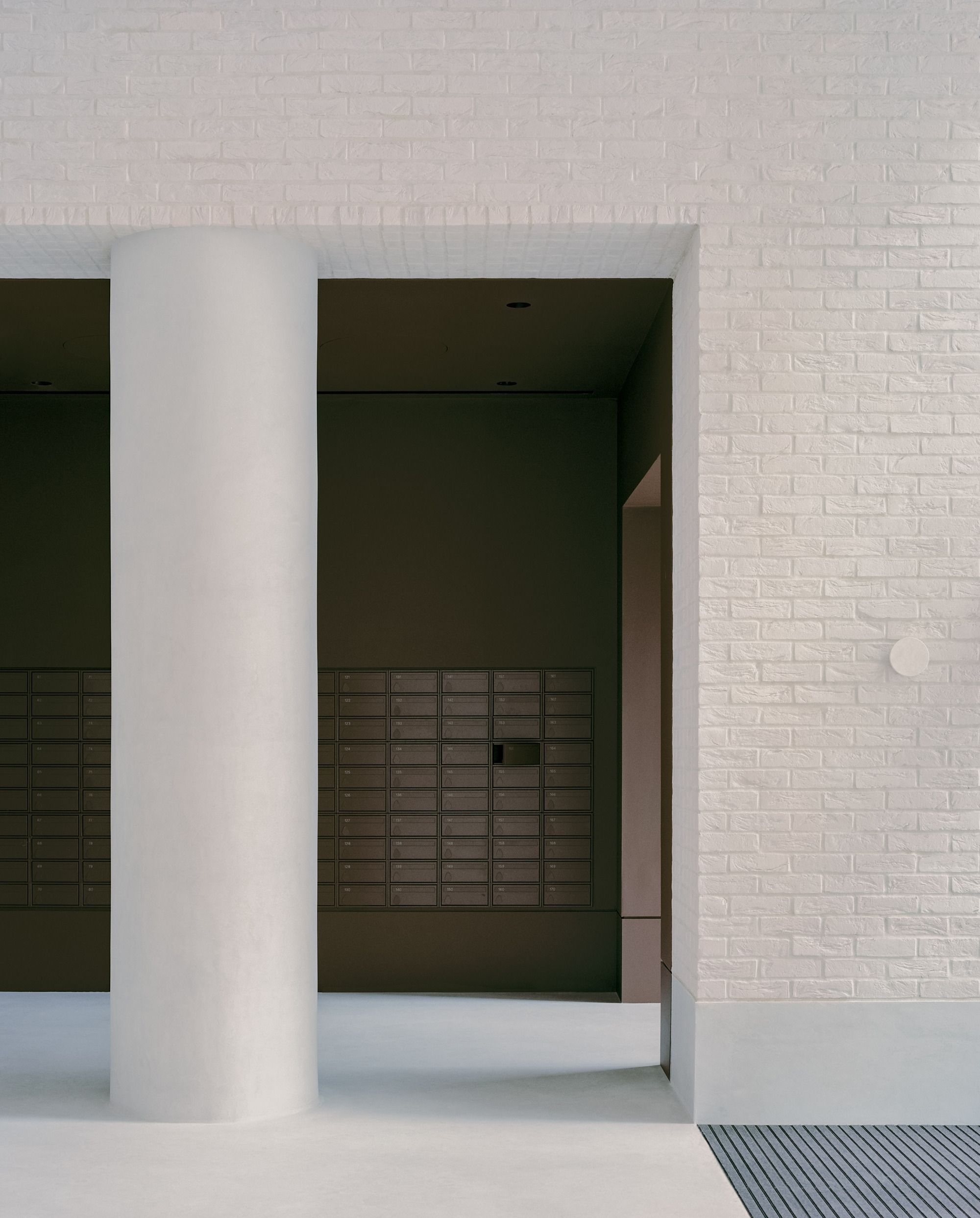 Covered entrance with white circular column framing a view into a dark vestibule with mailboxes