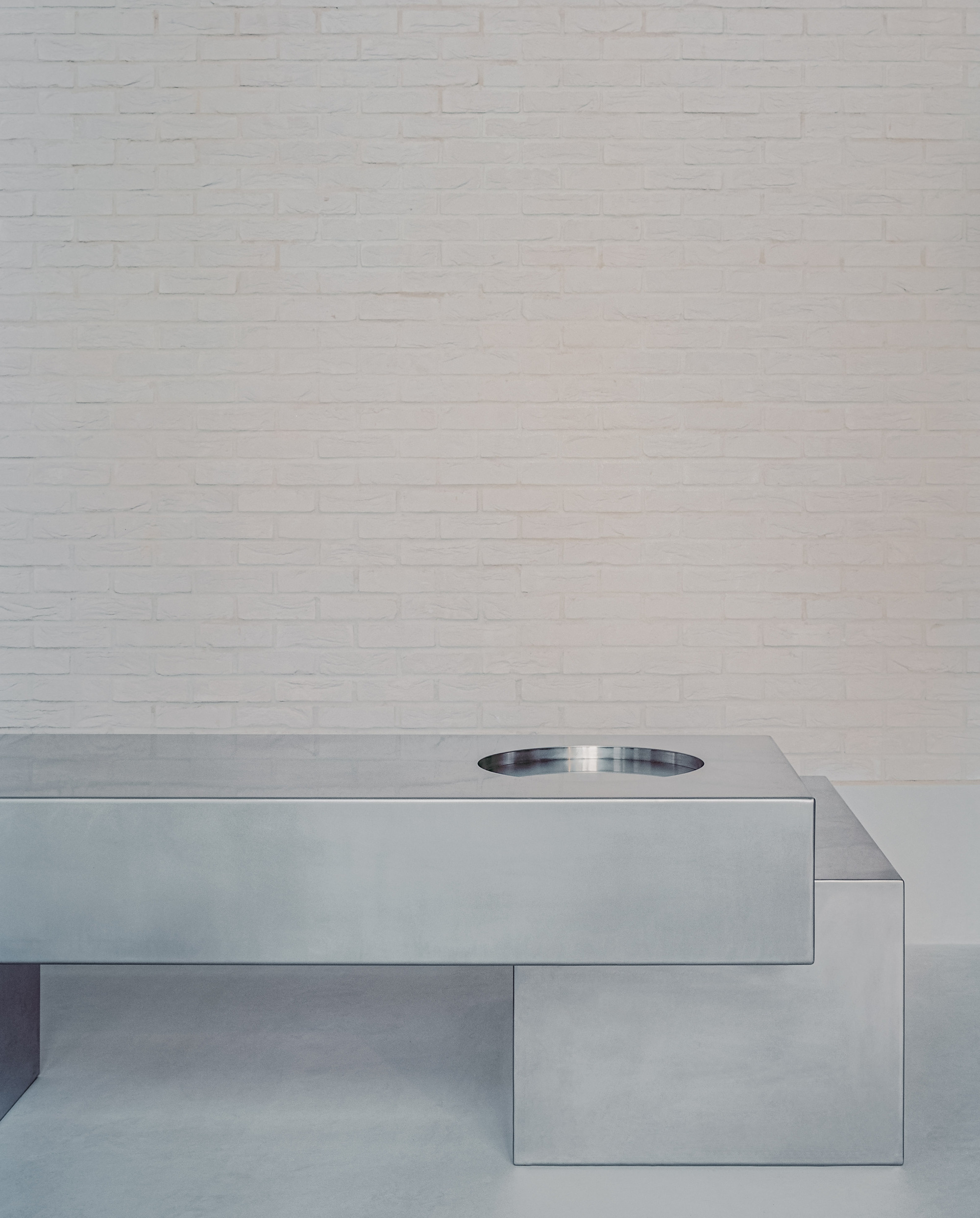Cantilevered stainless steel countertop with circular basin against white painted brick wall