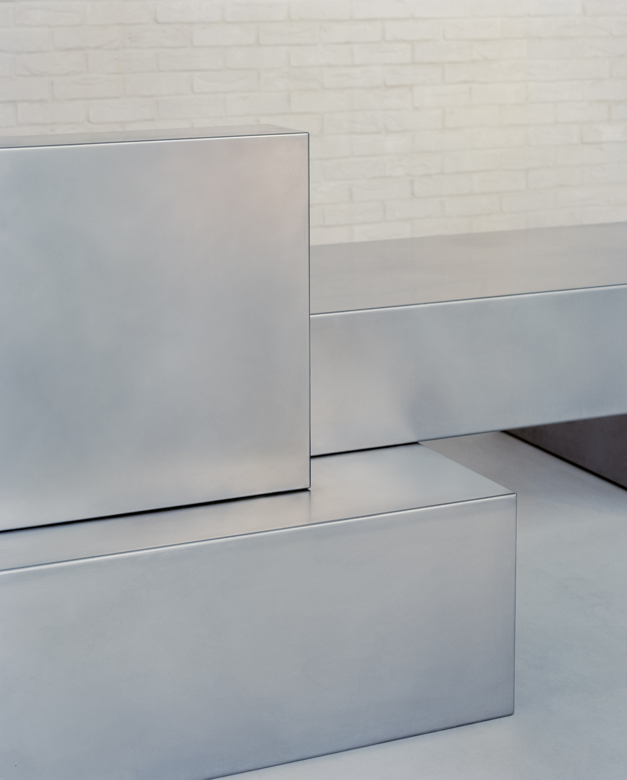 Detail of stainless steel counter edges and joints meeting white brick wall and grey flooring