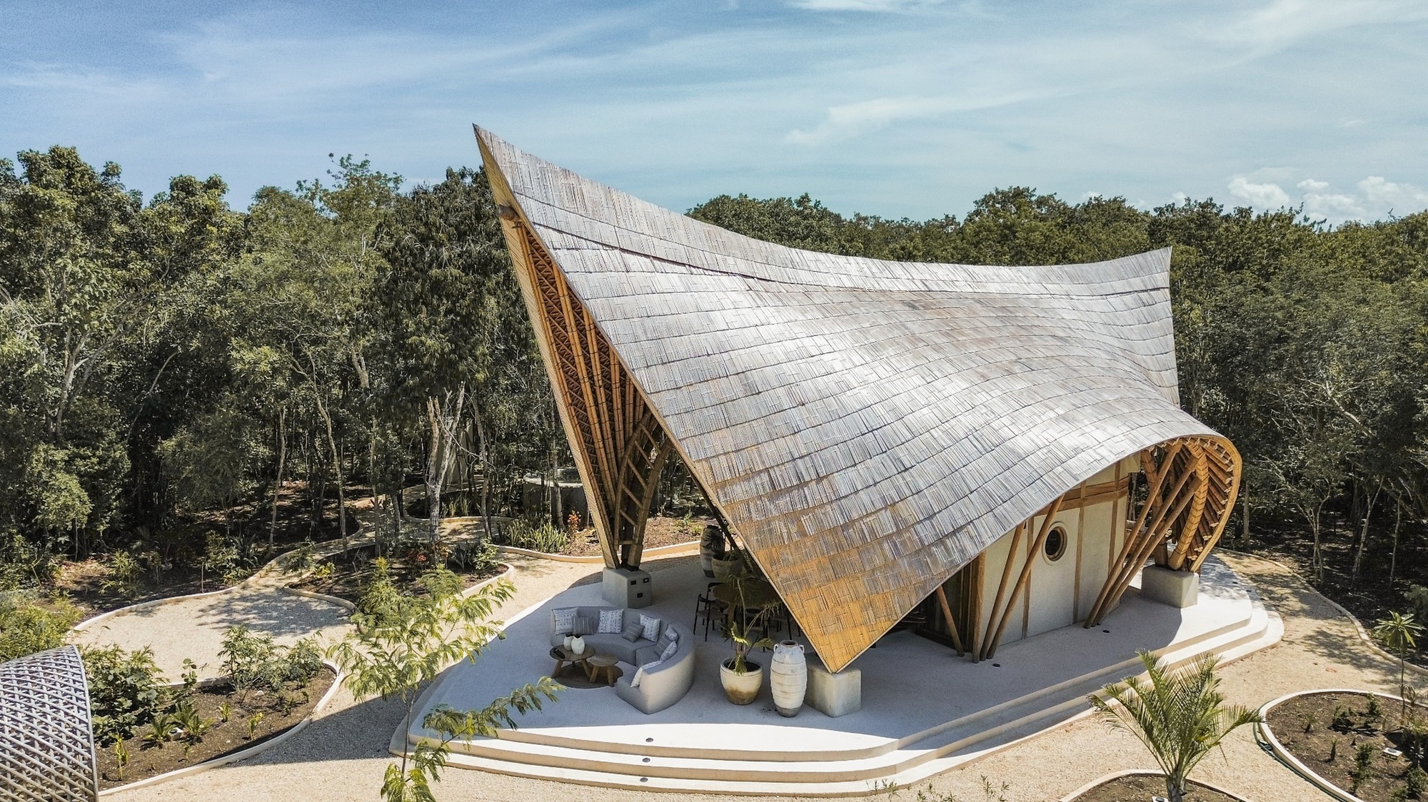 Aerial view of the sweeping shingled roof rising above a concrete terrace surrounded by dense trees