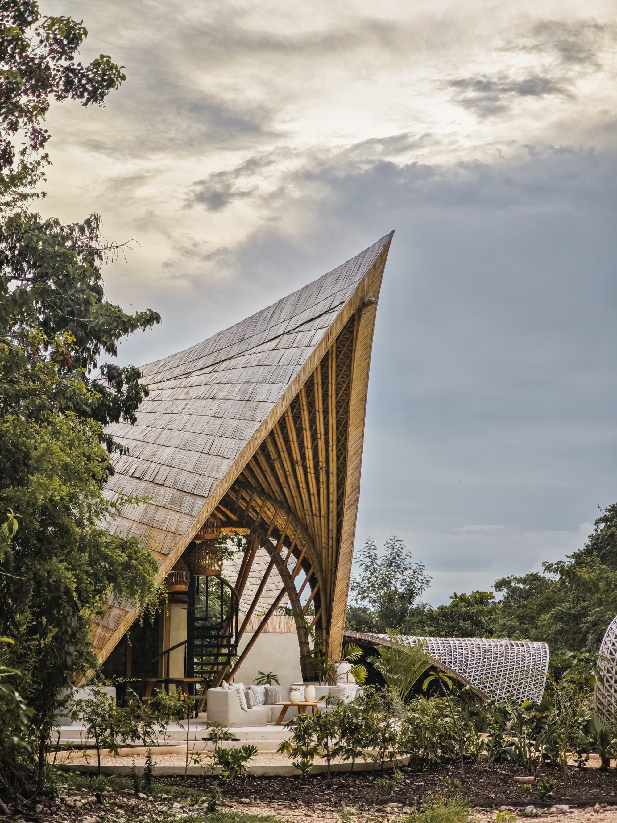 Side view of the curved shingled roof and radiating structural beams under a cloudy sky