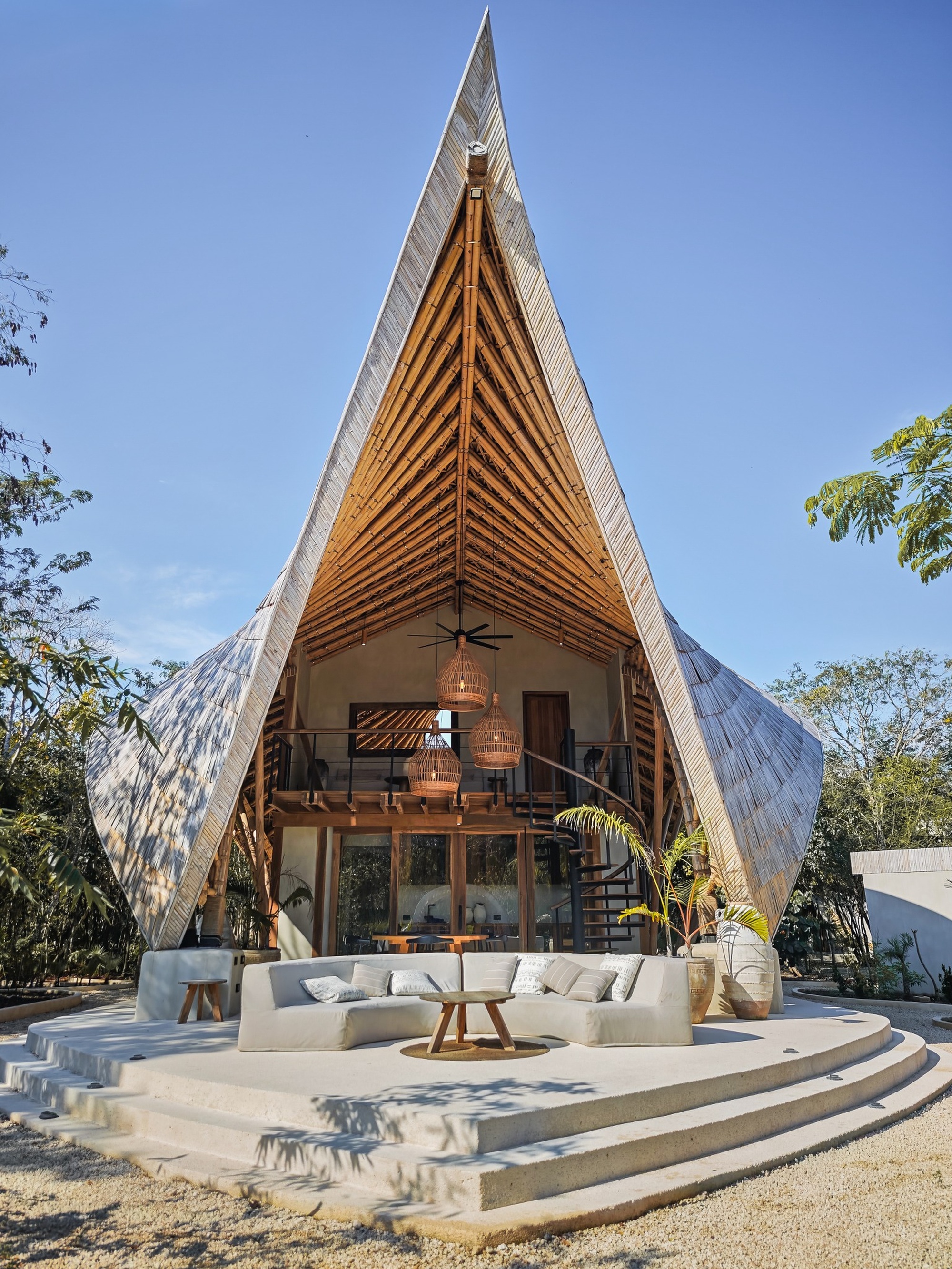 Front elevation showing the triangular gable end with timber louvers above stepped concrete terraces in sunlight
