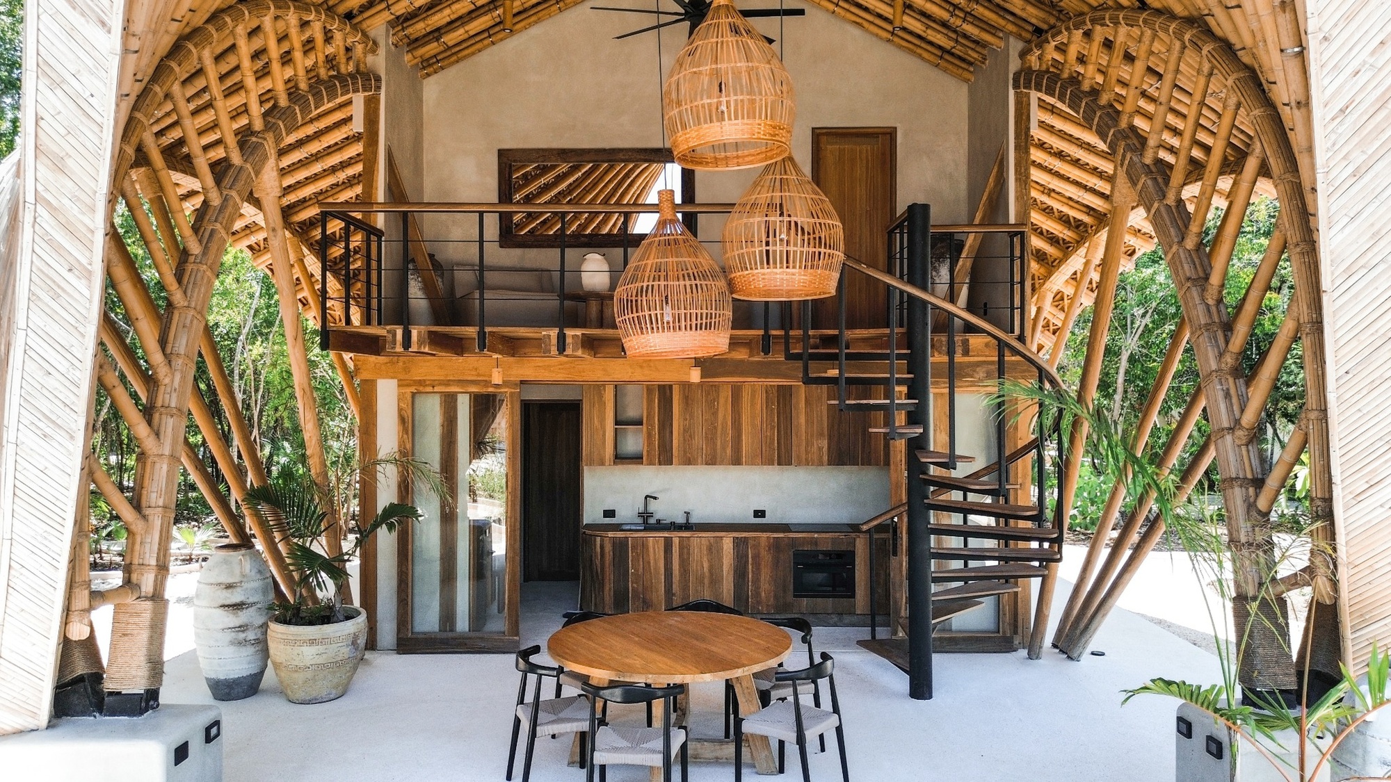Interior showing the double-height space with exposed bamboo roof structure, spiral stair, mezzanine kitchen and woven pendant lights