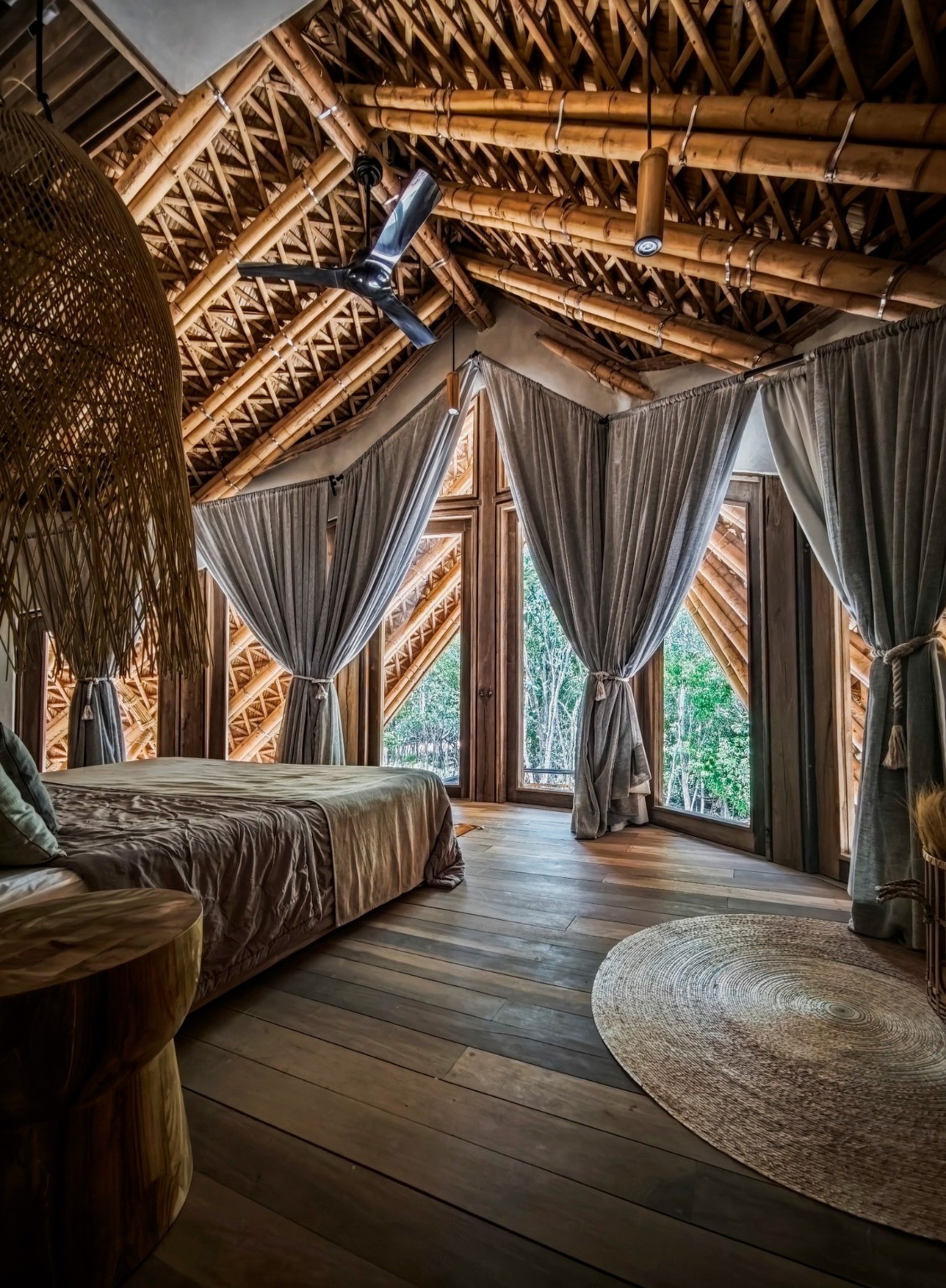Bedroom with exposed bamboo lattice ceiling, draped curtains on timber-framed openings and dark timber plank flooring