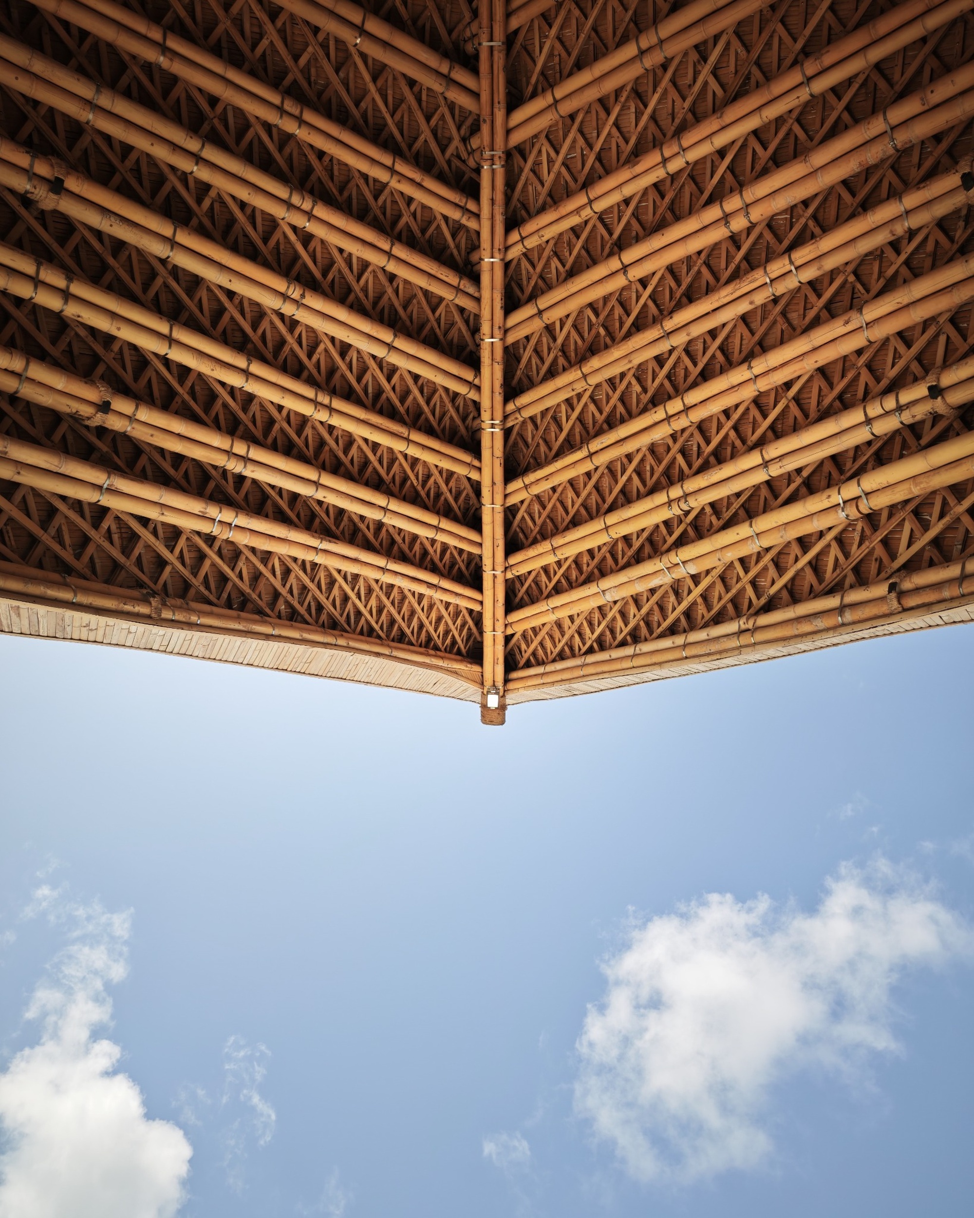 Underside view of the shingled bamboo roof peak with lattice bracing against a partly cloudy sky