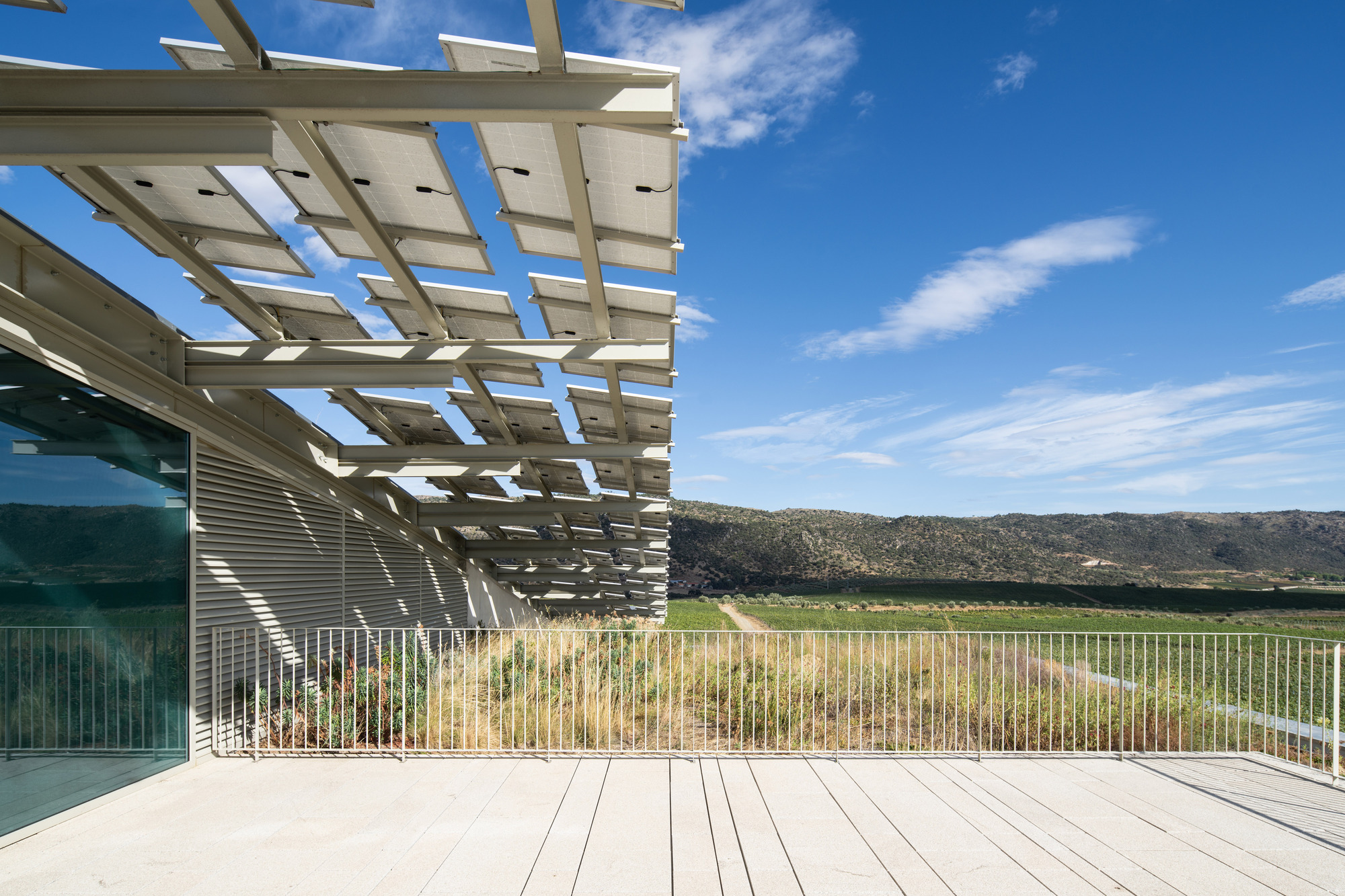 Timber pergola shading a white deck terrace overlooking cultivated fields under blue sky