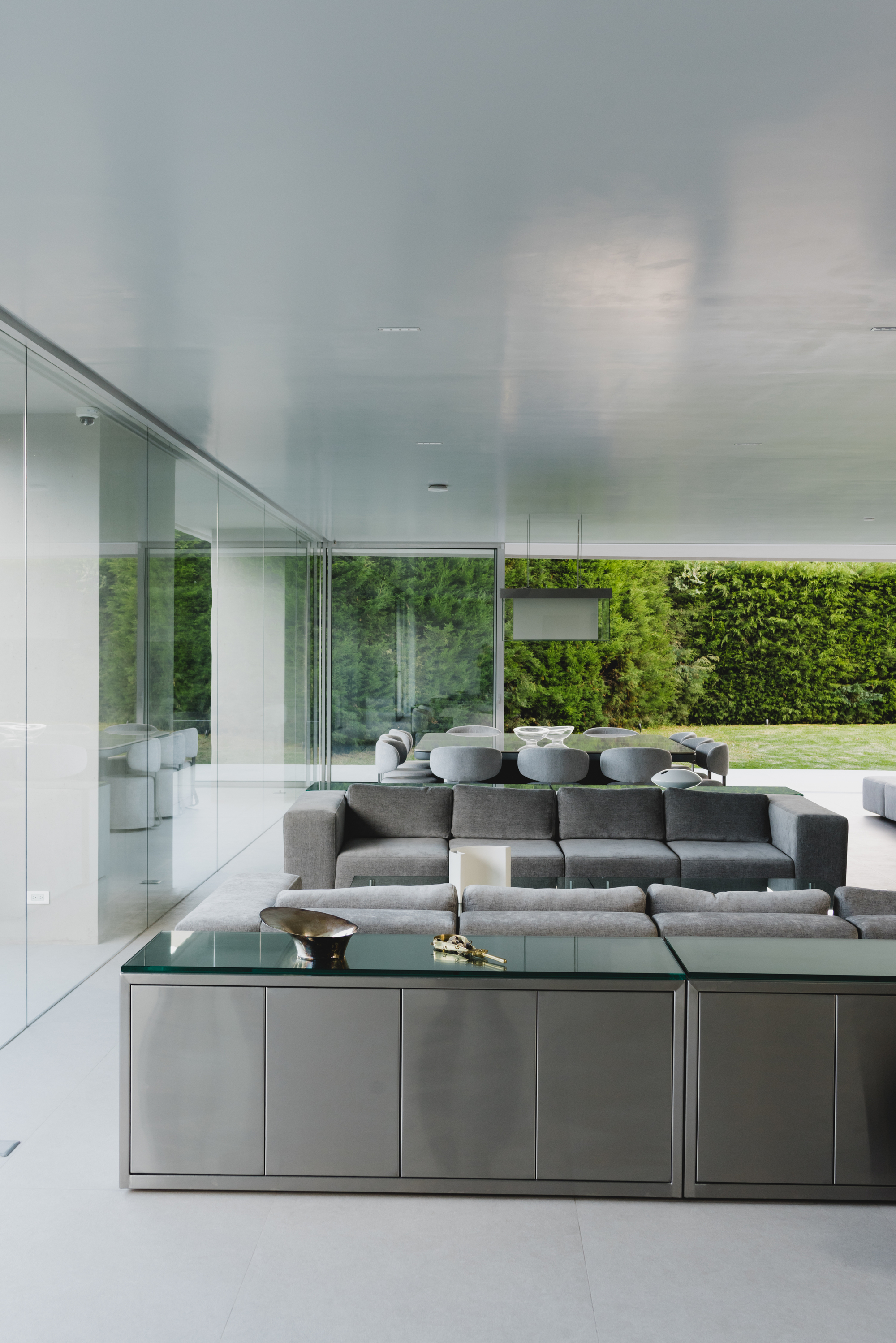 Open plan living area with floor-to-ceiling glass walls overlooking the lawn and garden hedge
